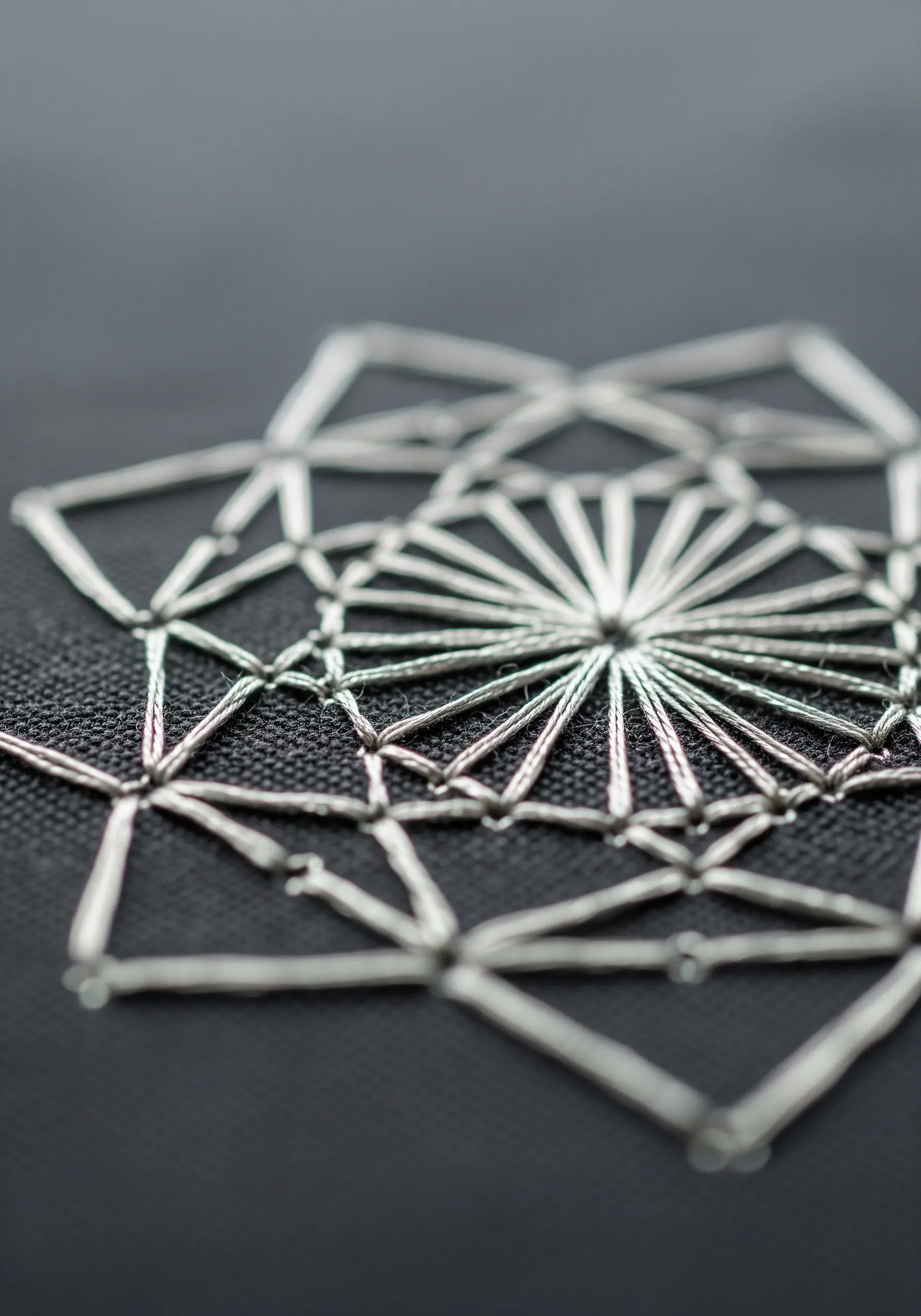 A close-up of a silver geometric mandala stitched on black fabric.