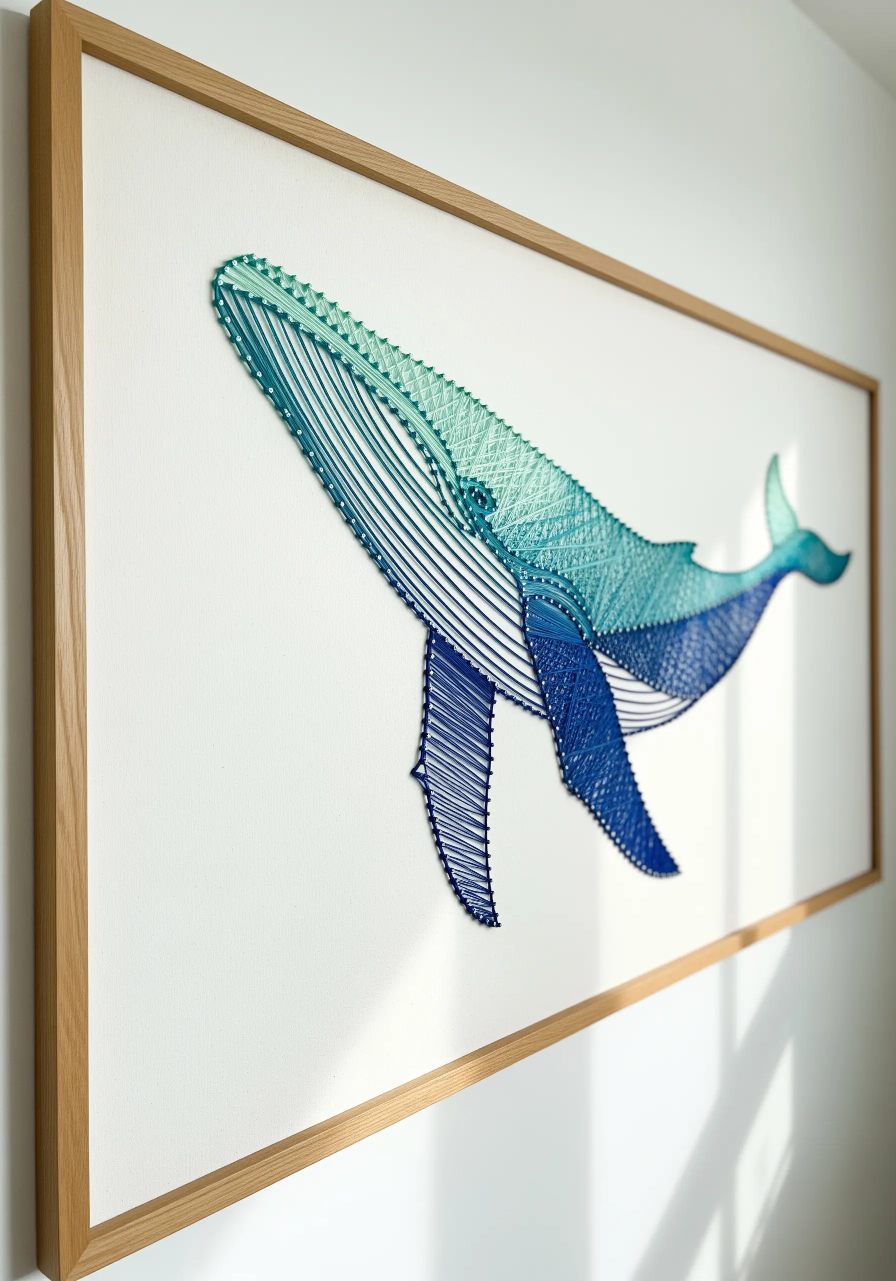 Blue and green gradient embroidery of a humpback whale in a light wood frame.