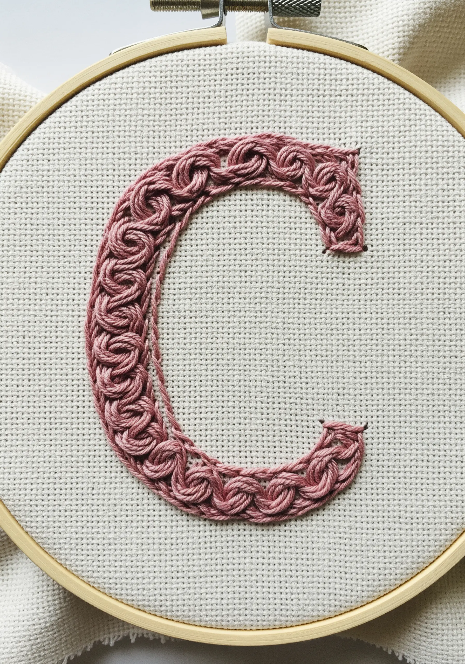 Letter 'C' filled with an intricate pink woven or knotted stitch.