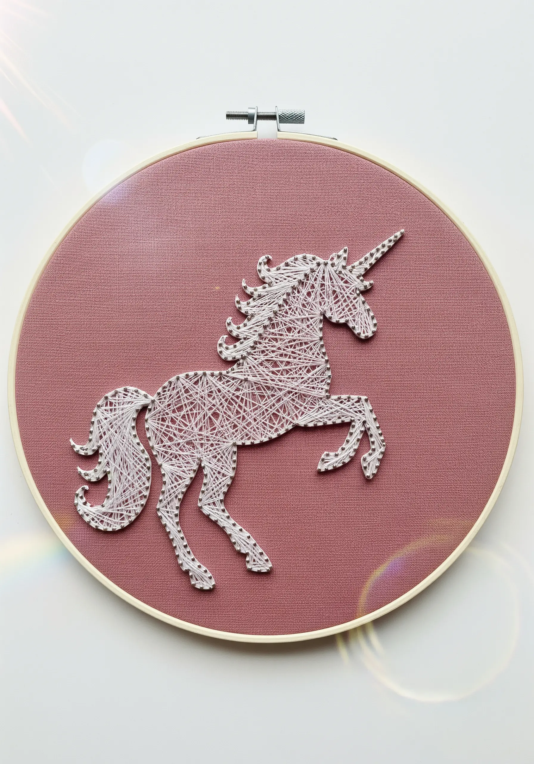 Delicate white thread embroidery of a unicorn silhouette on a dusty rose fabric.
