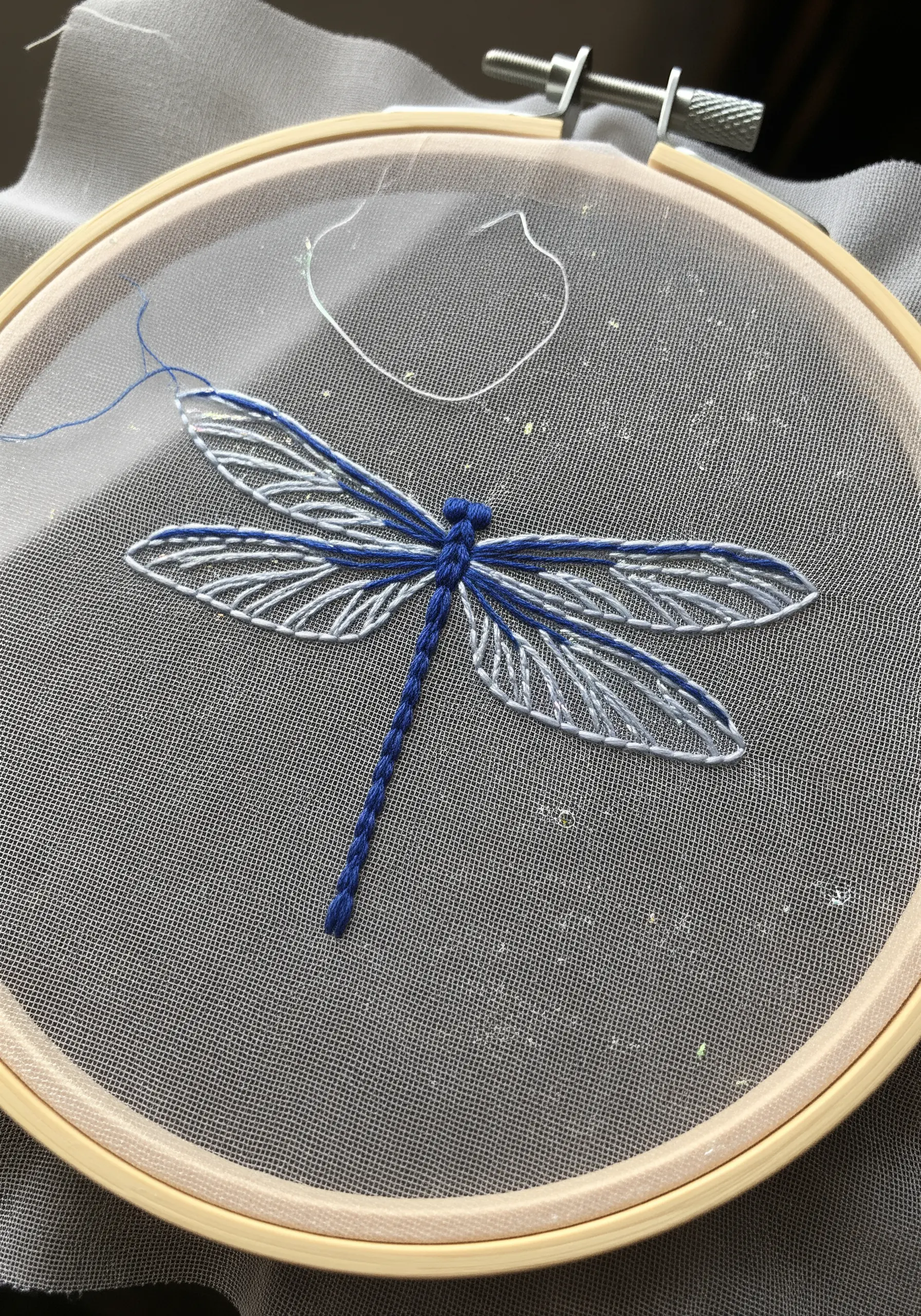 A dragonfly with blue and white wings embroidered on sheer, translucent fabric.