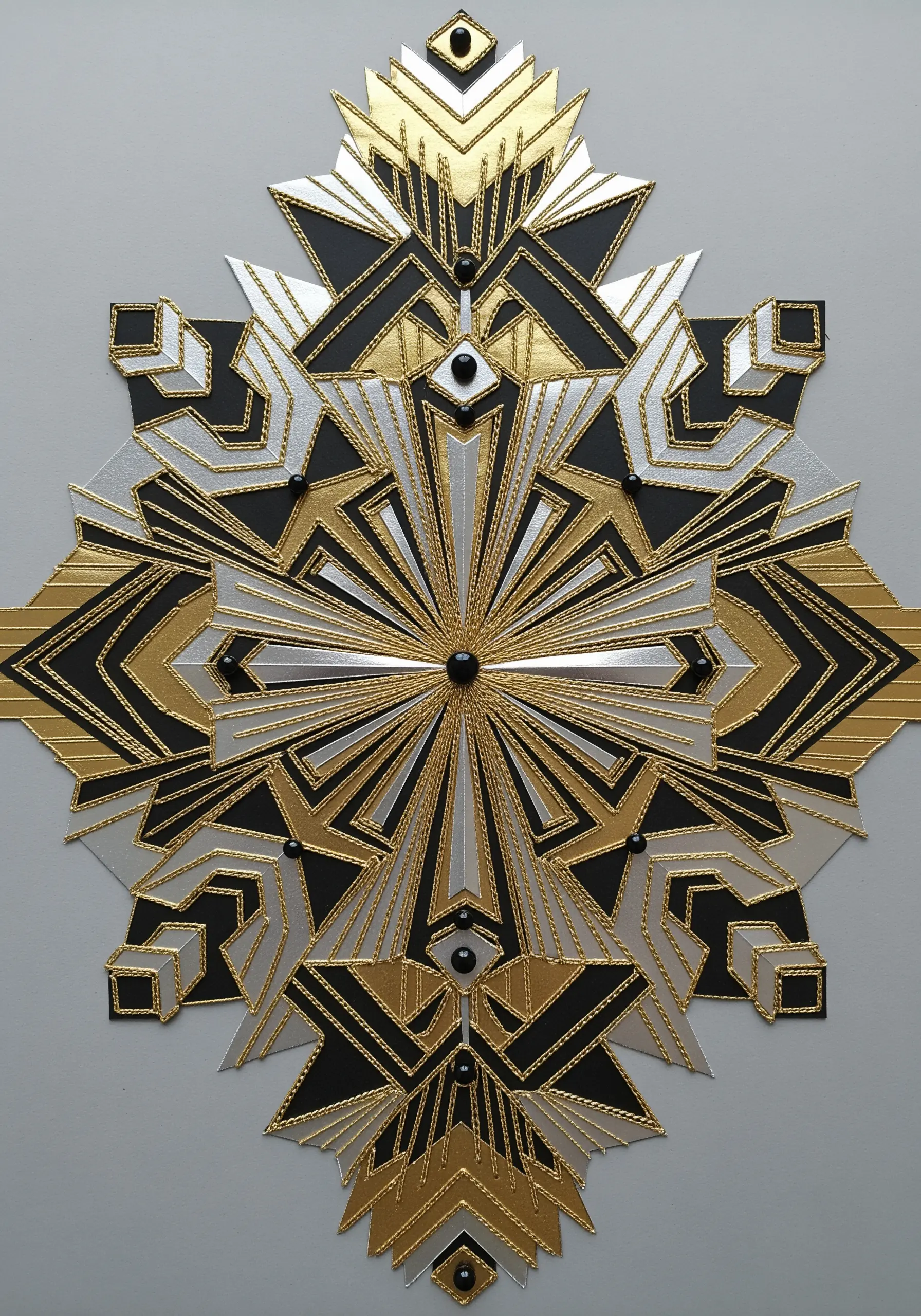 A symmetrical Art Deco design in black, gold, and silver paper with radiating gold stitches.