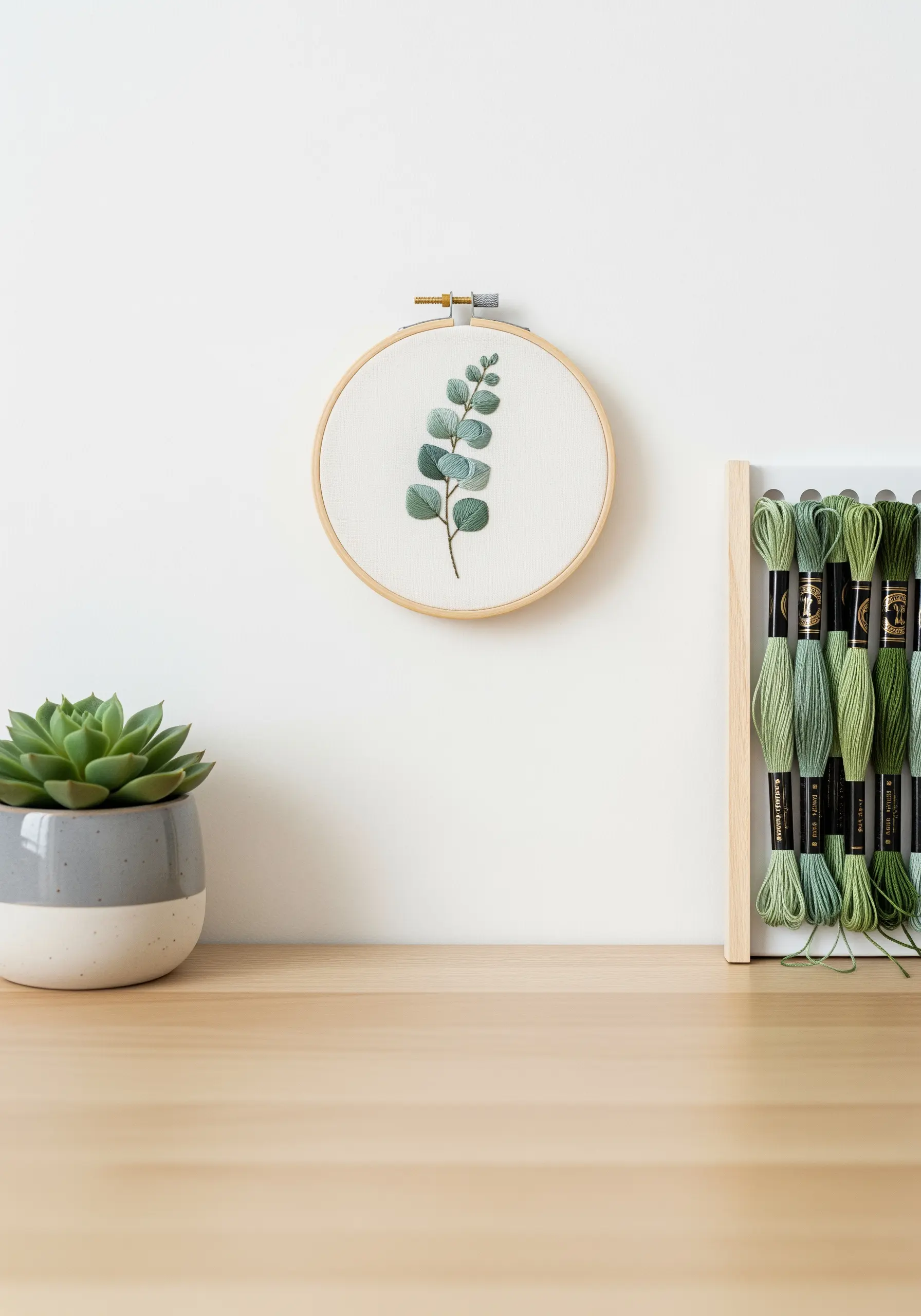 Realistic eucalyptus branch embroidered with subtle green thread gradients in a wooden hoop.