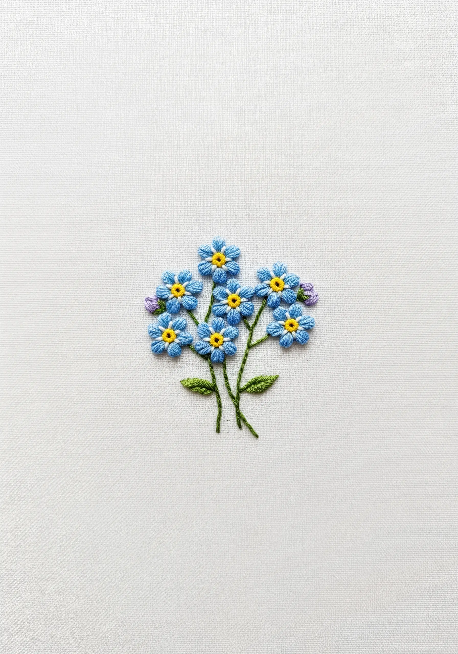 A small bouquet of blue forget-me-not flowers embroidered on white fabric.