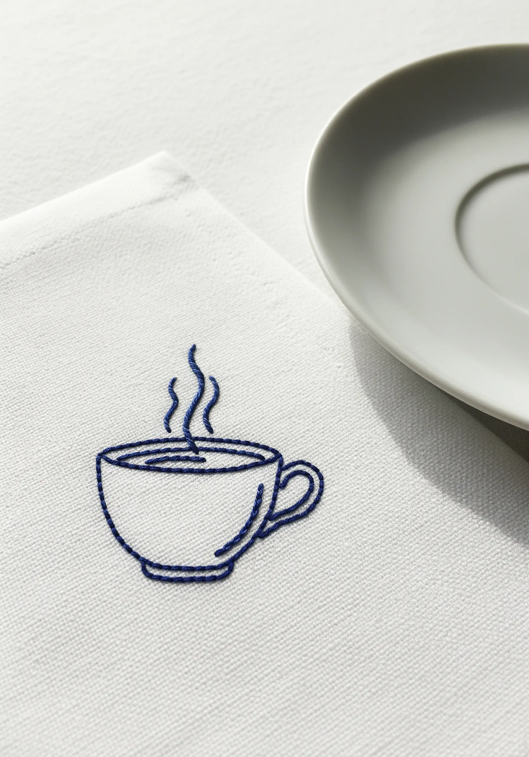 A minimal, single-color line art embroidery of a steaming coffee cup on a white napkin.
