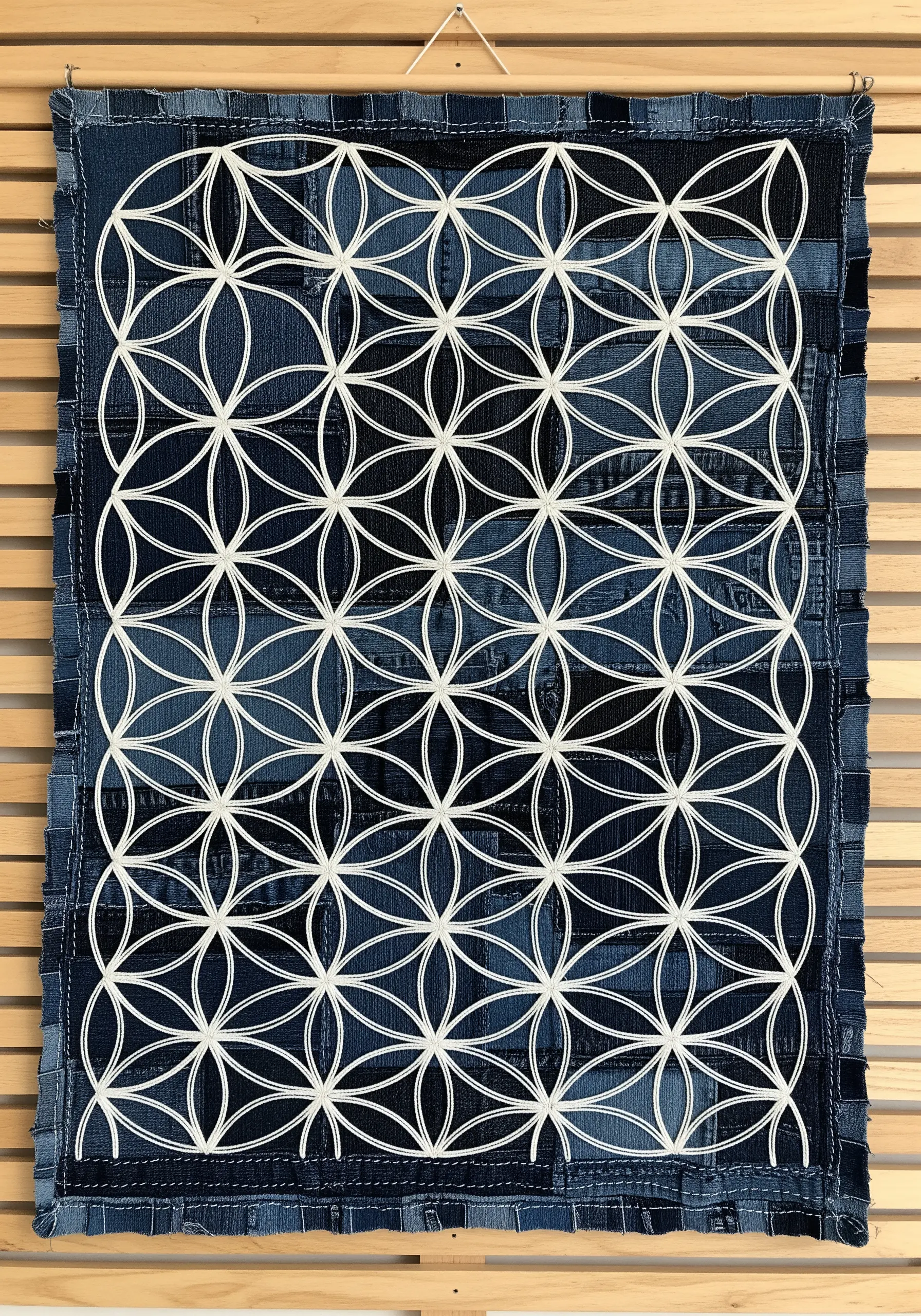 A geometric Flower of Life pattern created with reverse appliqué on a patchwork denim background.