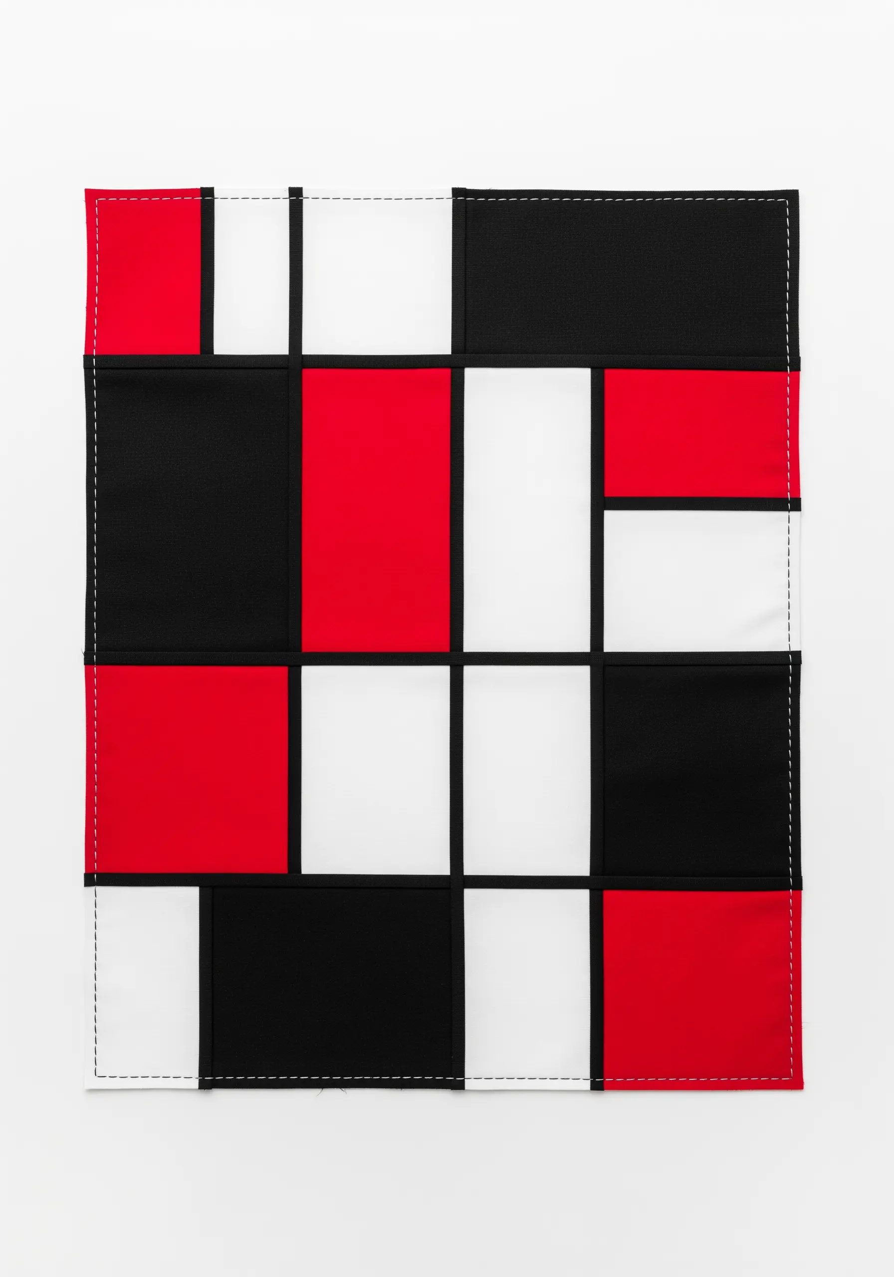 A modern, abstract fabric collage with red, black, and white squares in a Mondrian-style grid.