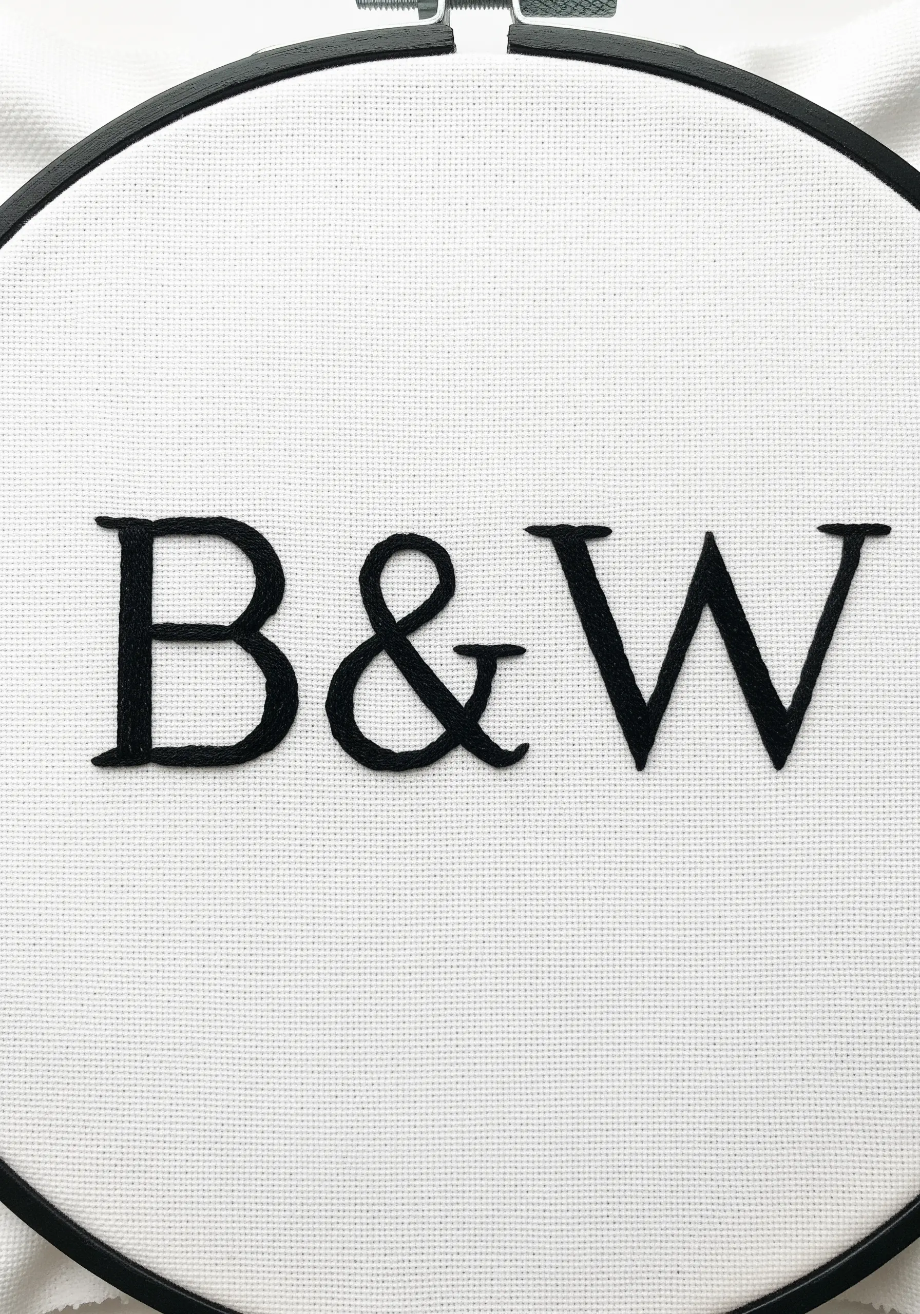 Black serif initials 'B&W' in satin stitch on white fabric.