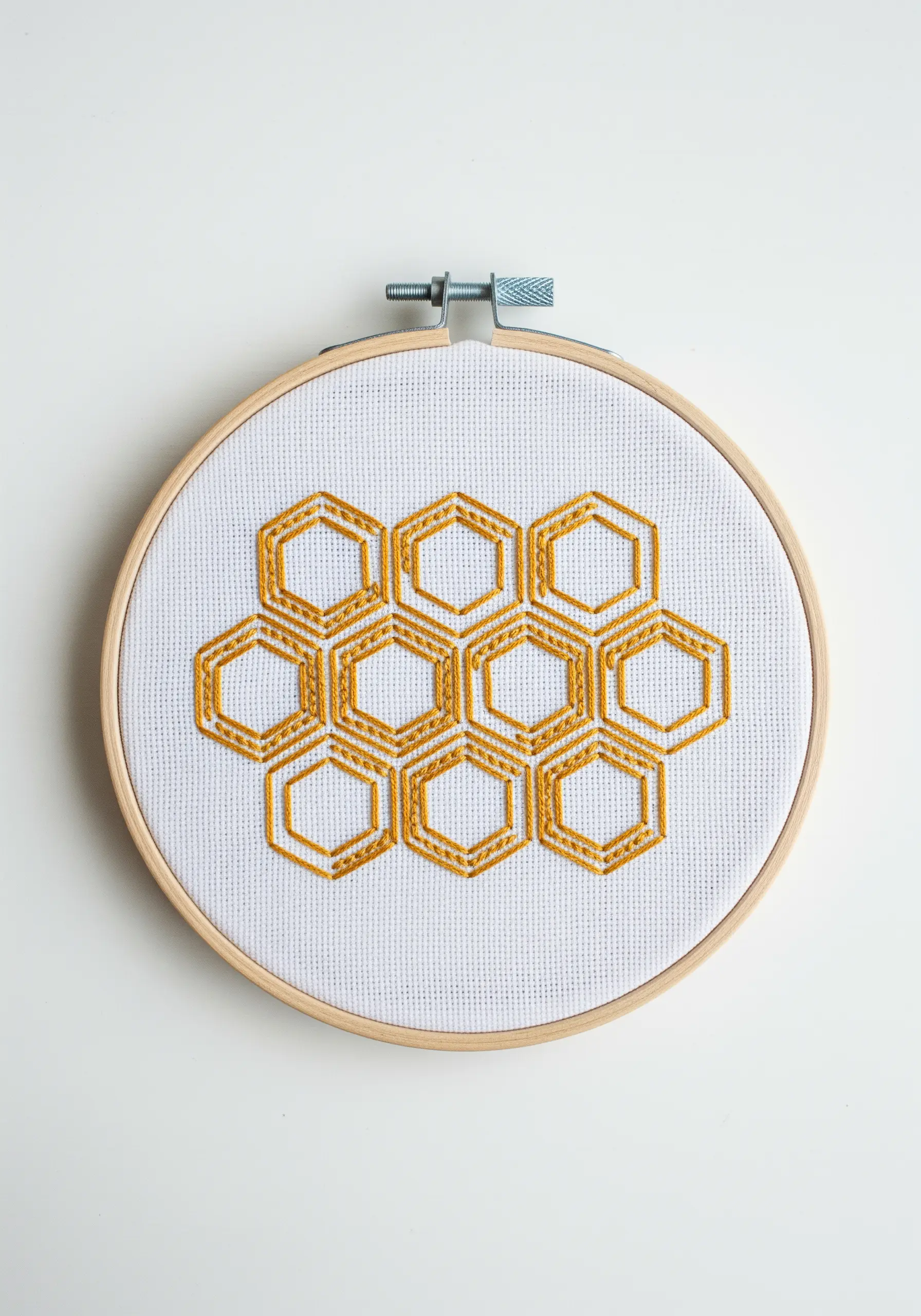 A geometric honeycomb pattern embroidered in golden yellow thread on white Aida cloth.