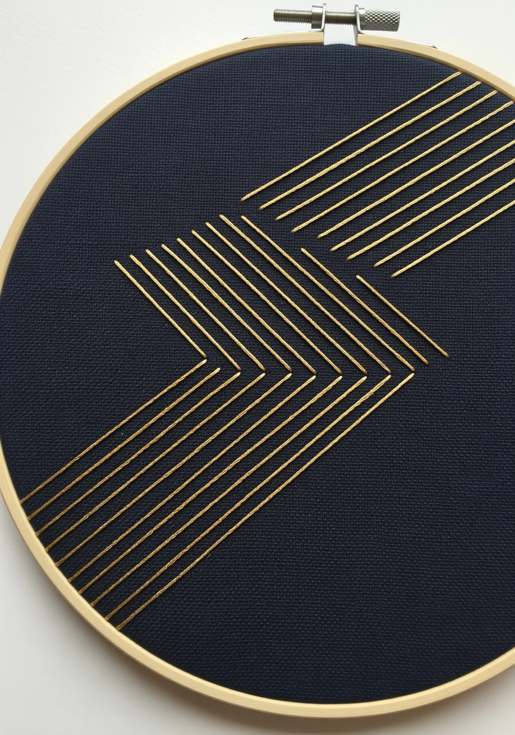 A sharp, geometric arrow design stitched in gold metallic thread on dark navy fabric.