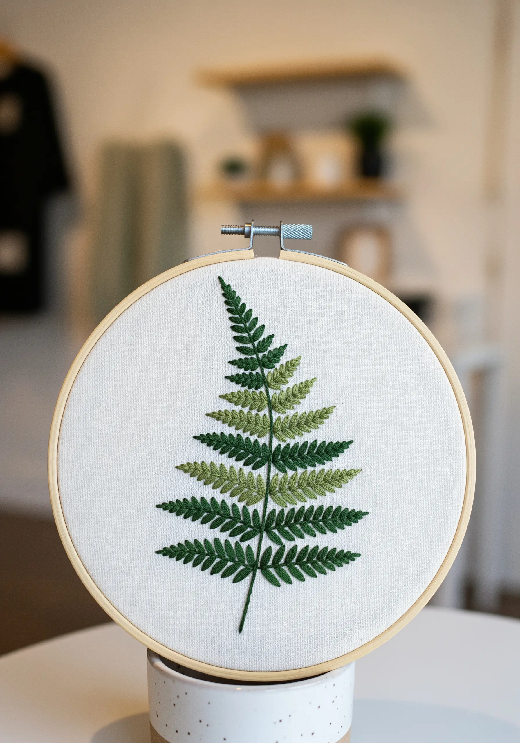 A single fern frond embroidered with a gradient of green shades on white fabric.