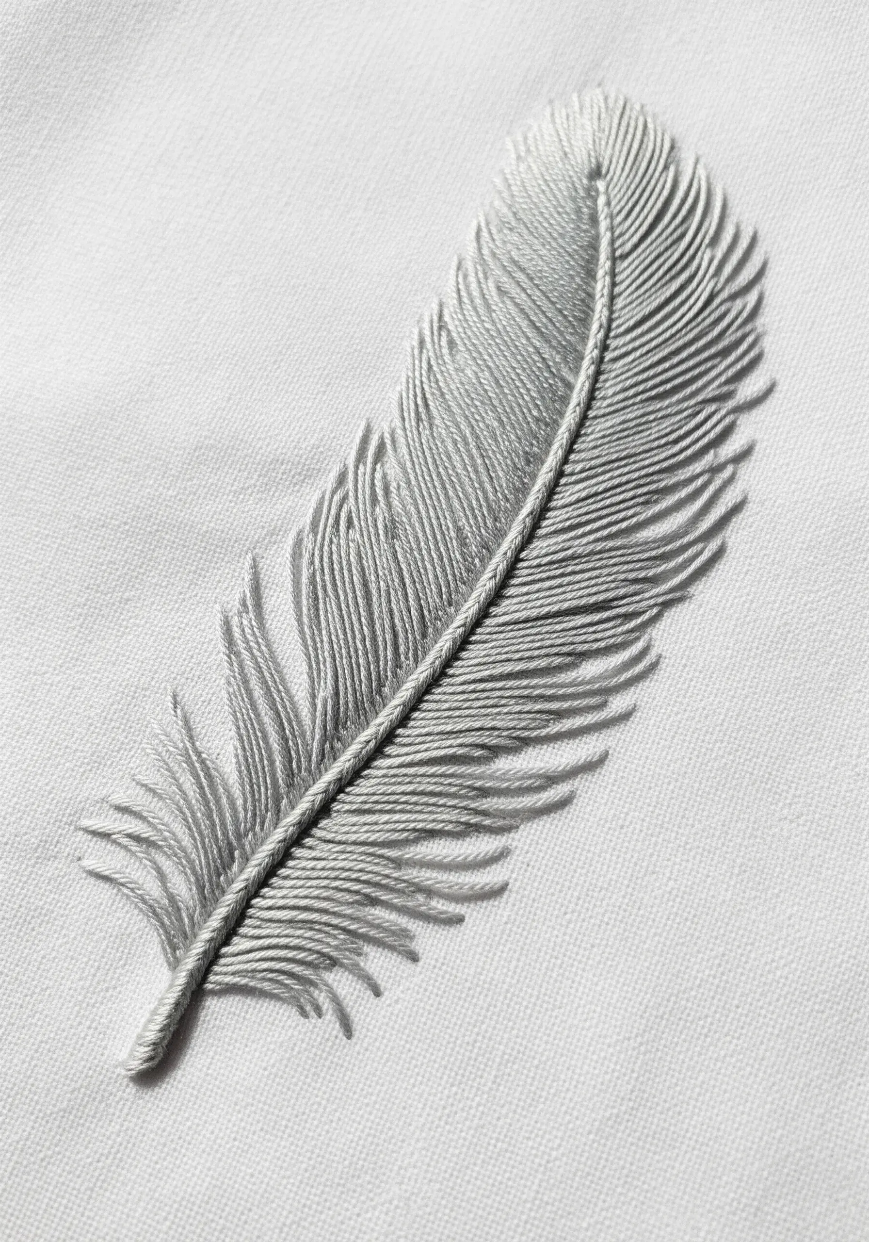 A delicate feather embroidered in light gray thread on a white fabric surface.