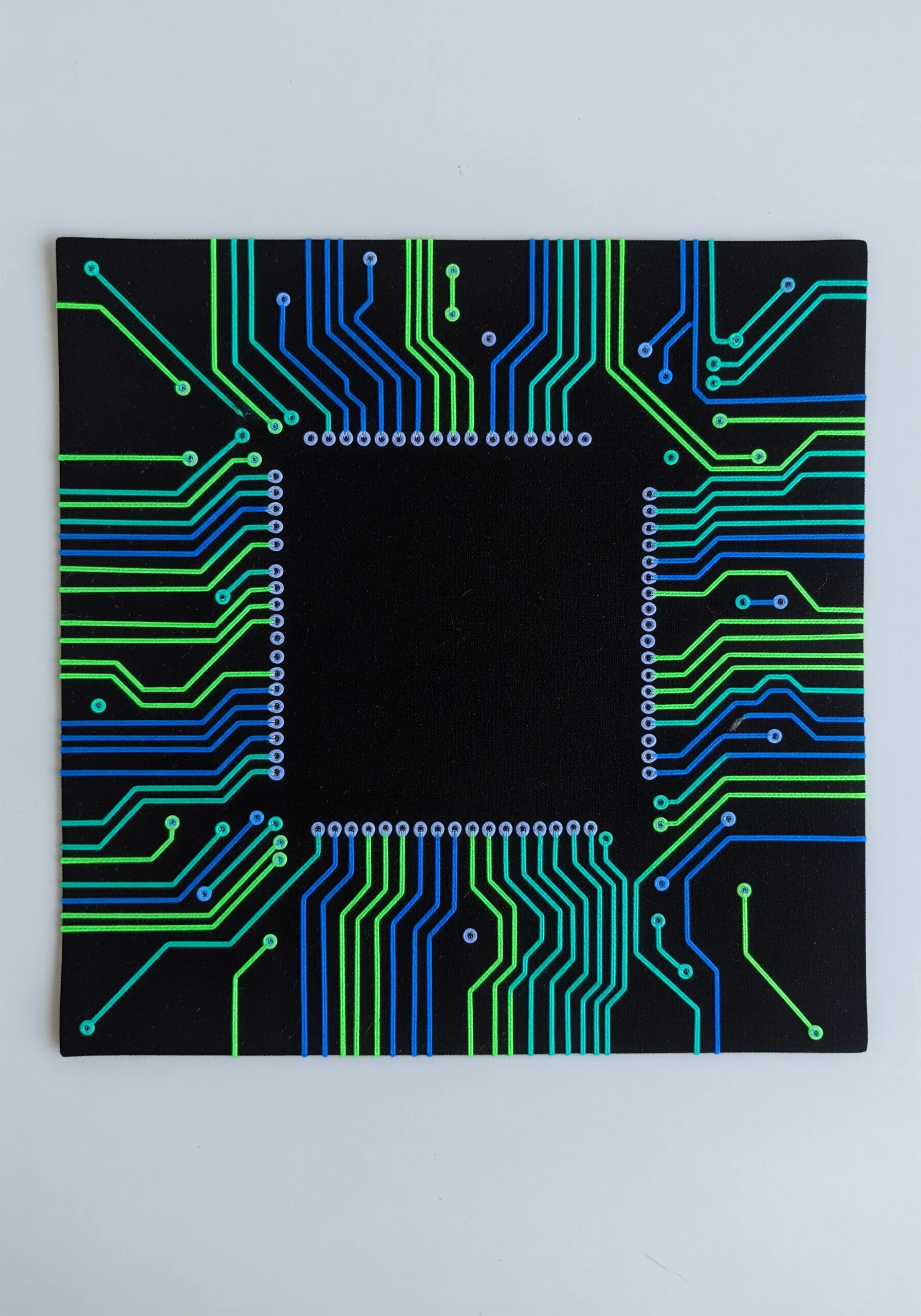 A circuit board pattern stitched in neat lines of blue and green neon thread.