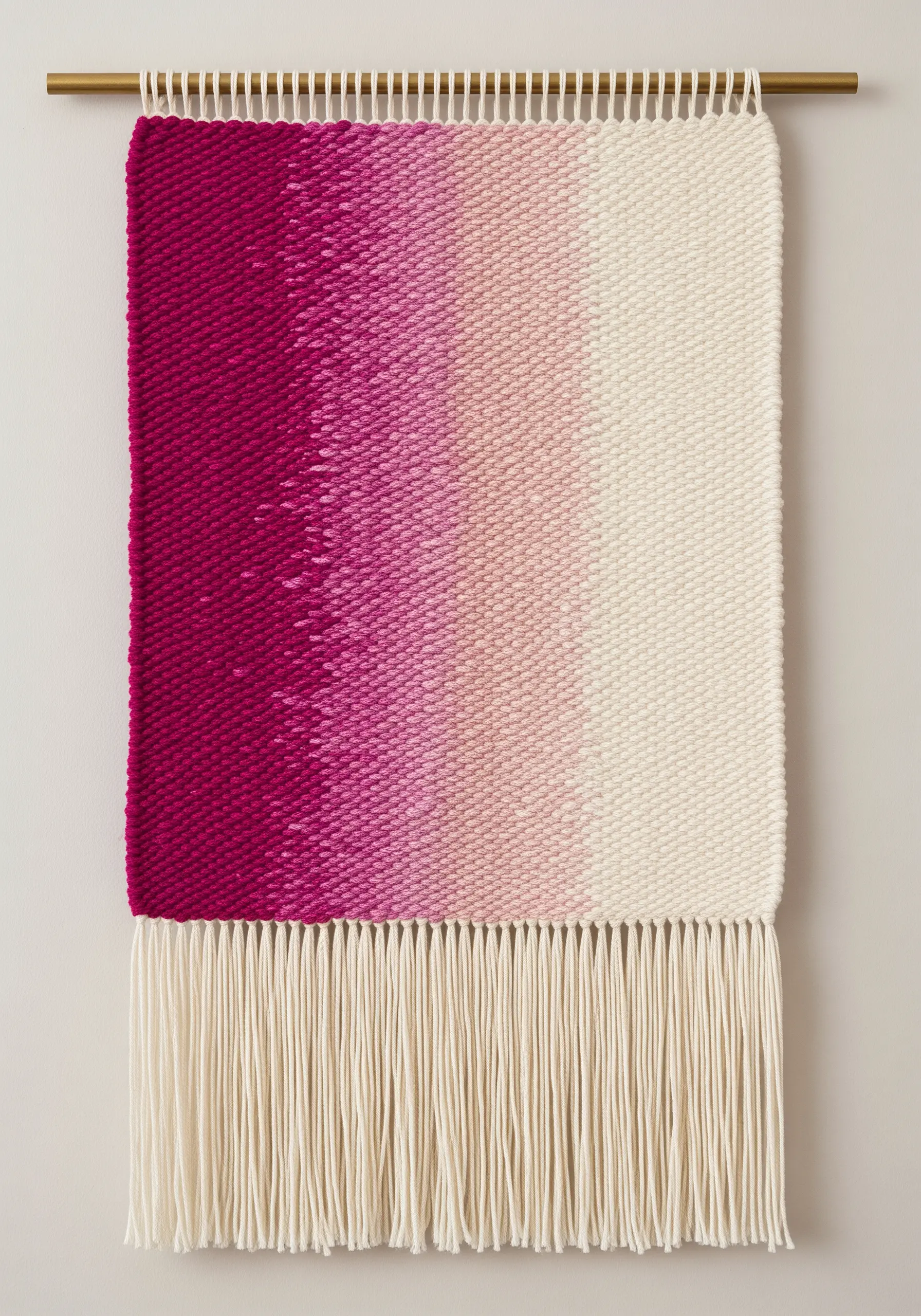 A woven wall hanging with a soft, blended gradient from deep pink to cream, with fringe.