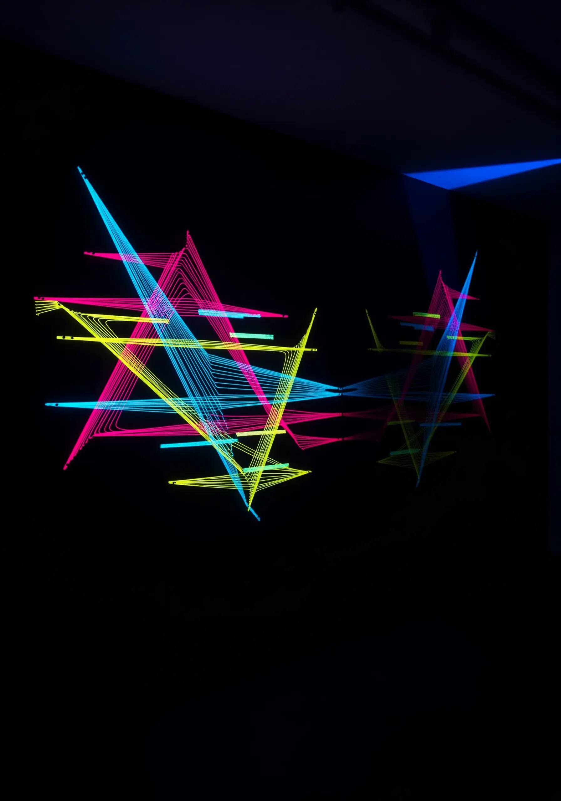 Geometric thread art in neon pink, yellow, and blue, glowing under a blacklight.