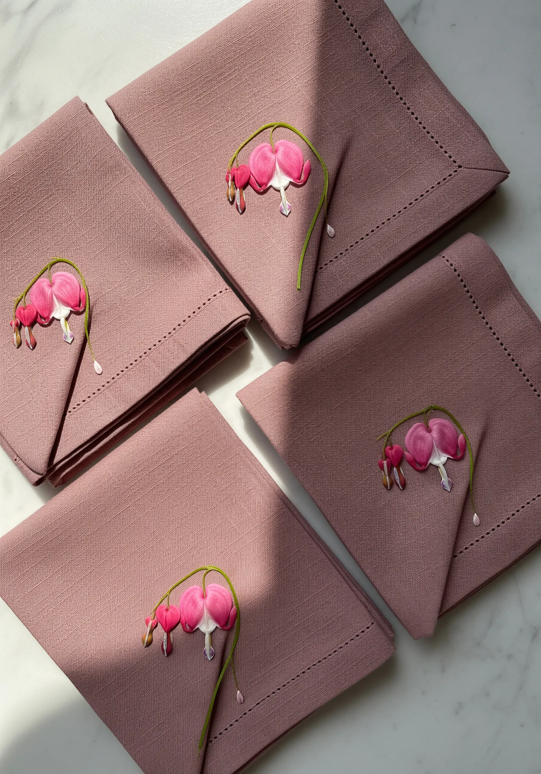 A set of dusty rose napkins, each embroidered with a small, delicate bleeding heart flower.