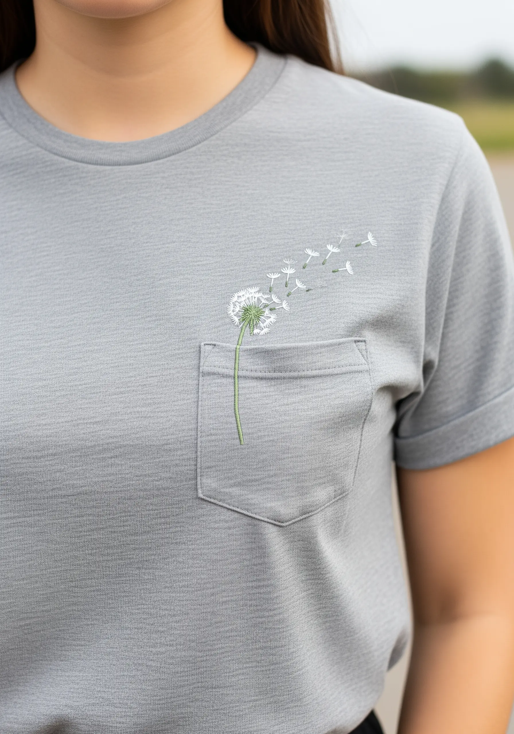 Small dandelion embroidered on a t-shirt pocket, with seeds floating out.