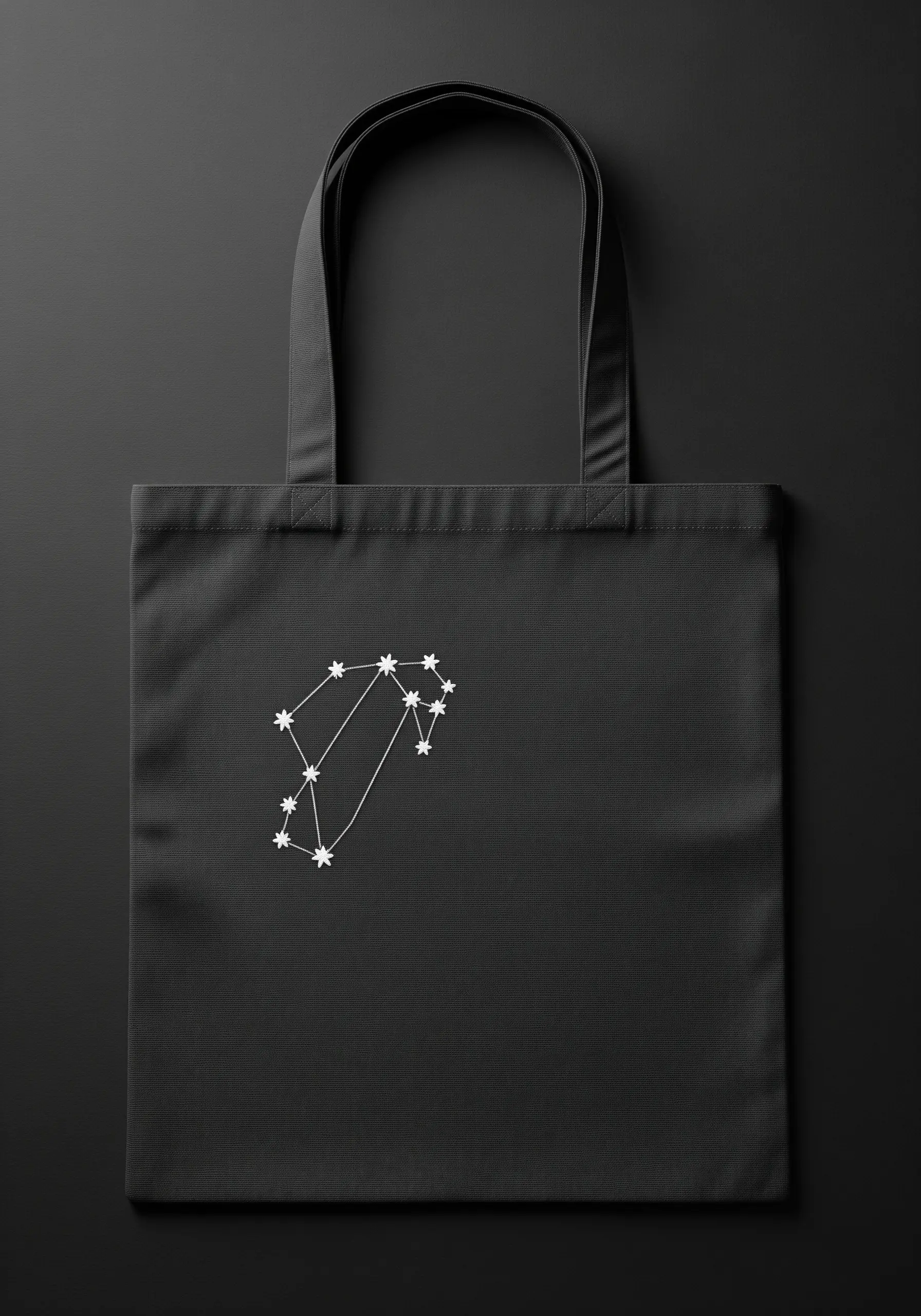 A white embroidered constellation design stitched on a plain black canvas tote bag.