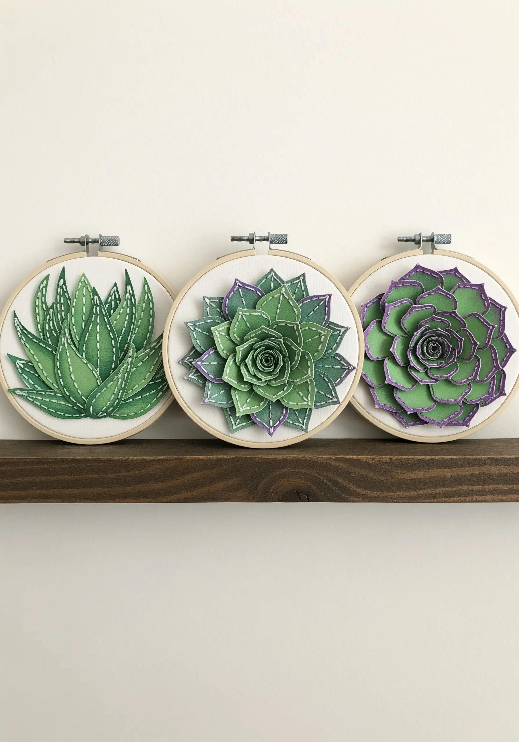Three embroidery hoops with layered paper succulents detailed with white running stitches.