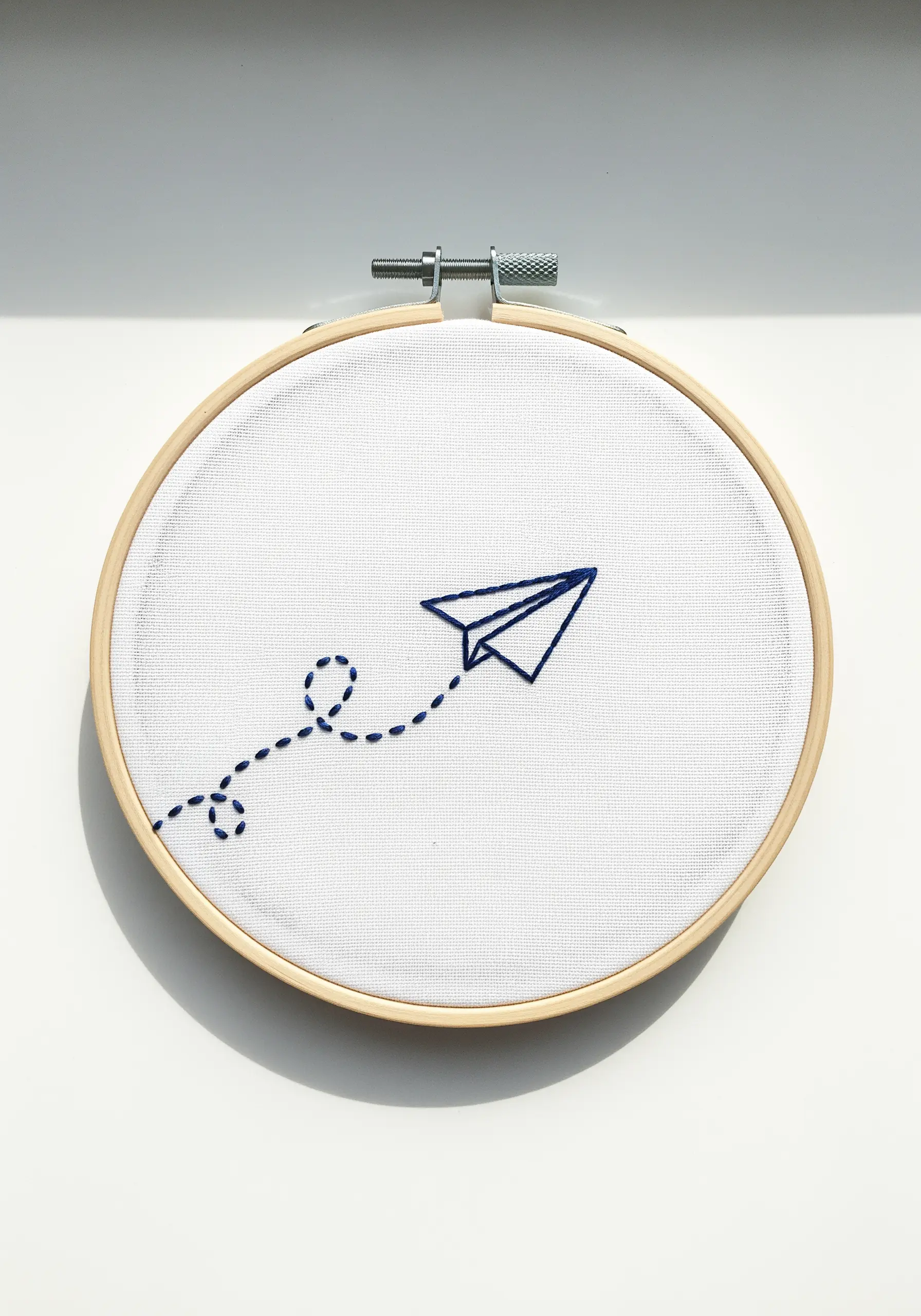 A simple paper airplane outlined in blue thread, followed by a looping dotted trail.