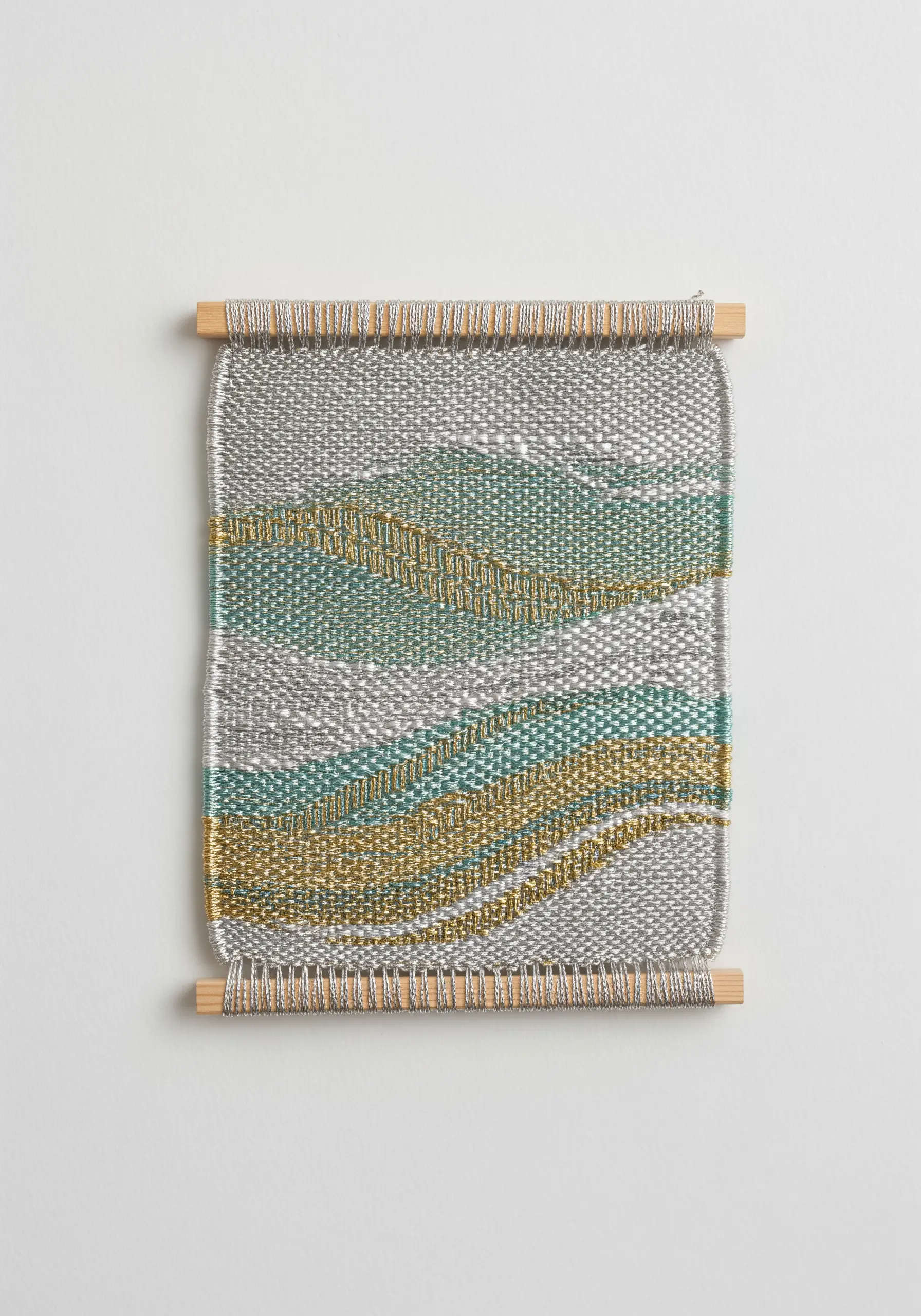 A small hand-woven piece with silver, gold, and teal threads creating a subtle shimmer.