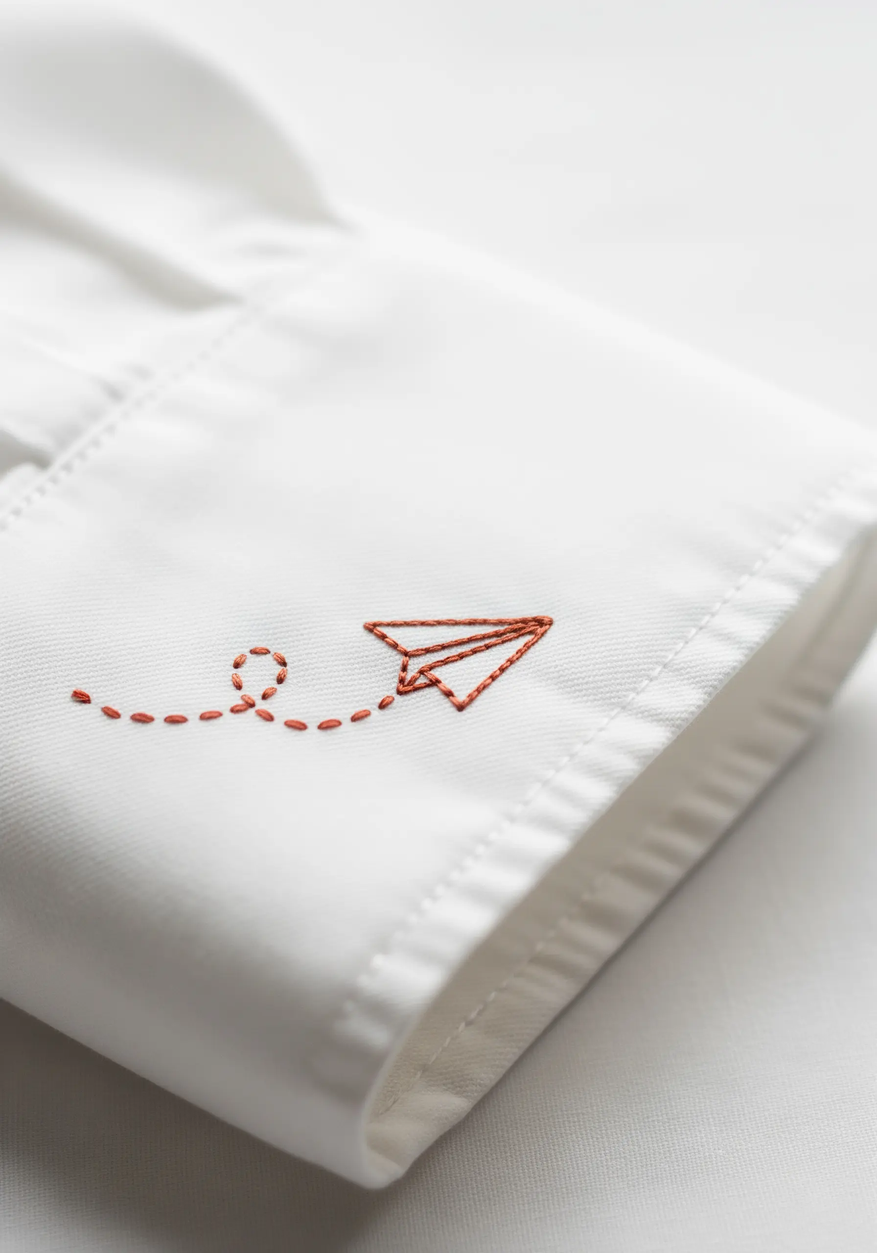A tiny orange paper airplane embroidered on the cuff of a crisp white dress shirt.