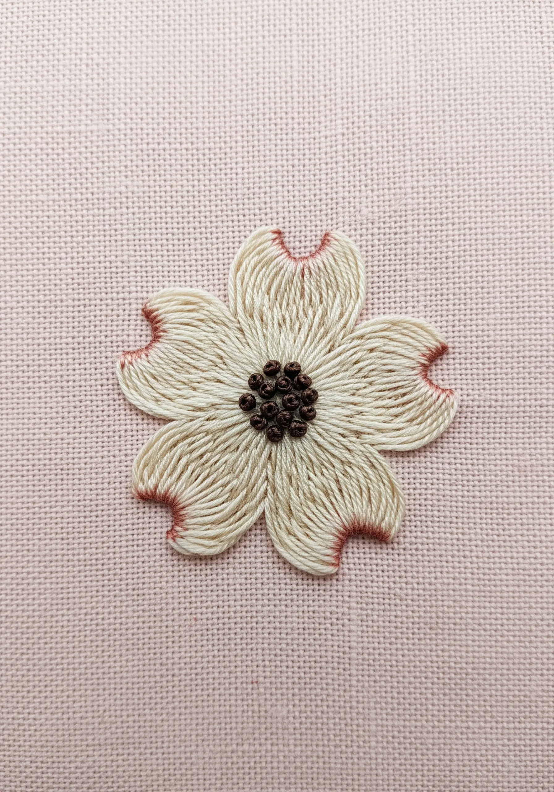 An embroidered dogwood flower with off-white petals tipped in reddish-brown.