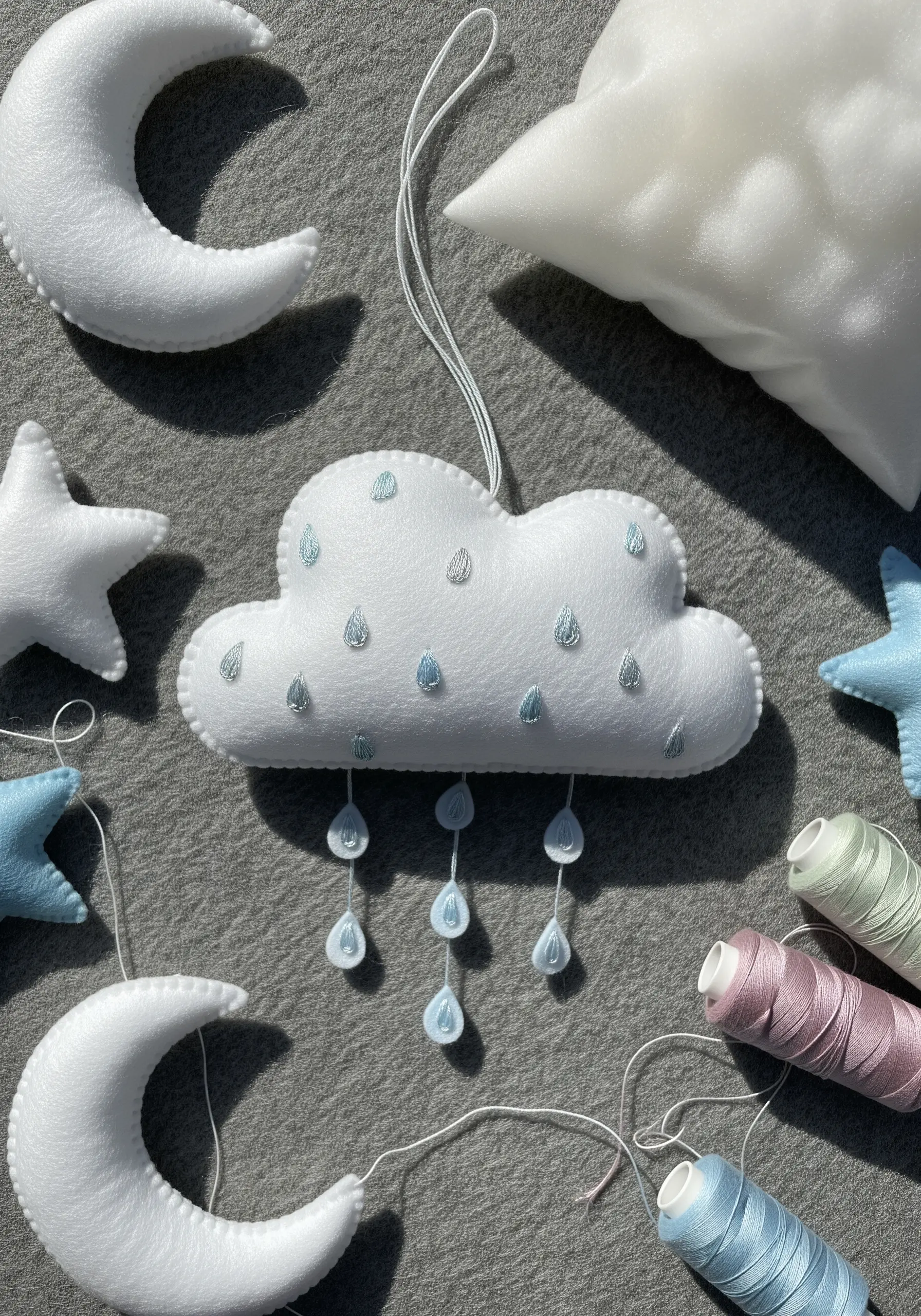 A handmade felt mobile with a cloud featuring tiny embroidered raindrops in metallic thread.