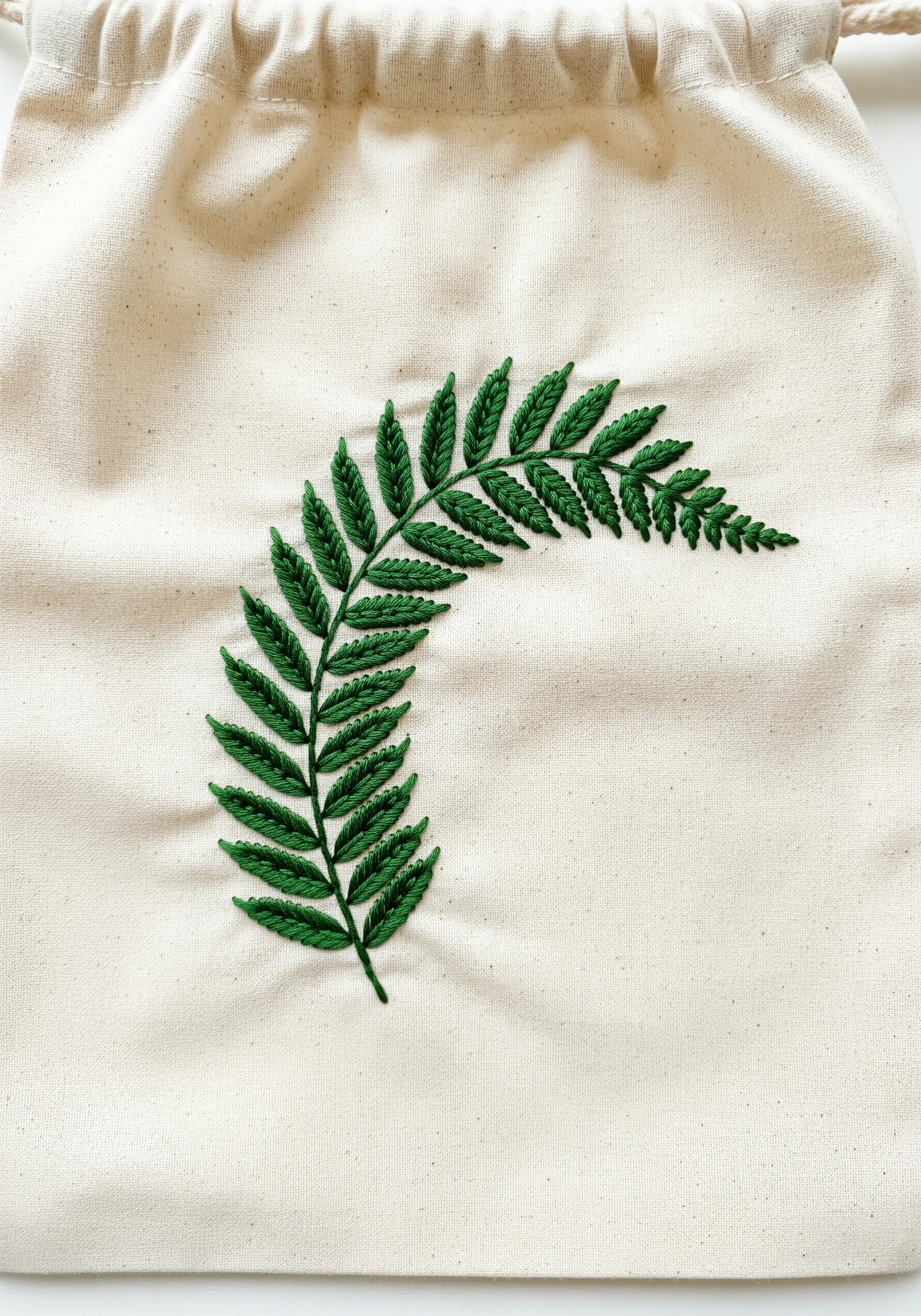 A lush green fern frond embroidered with textured French knots on a canvas bag.