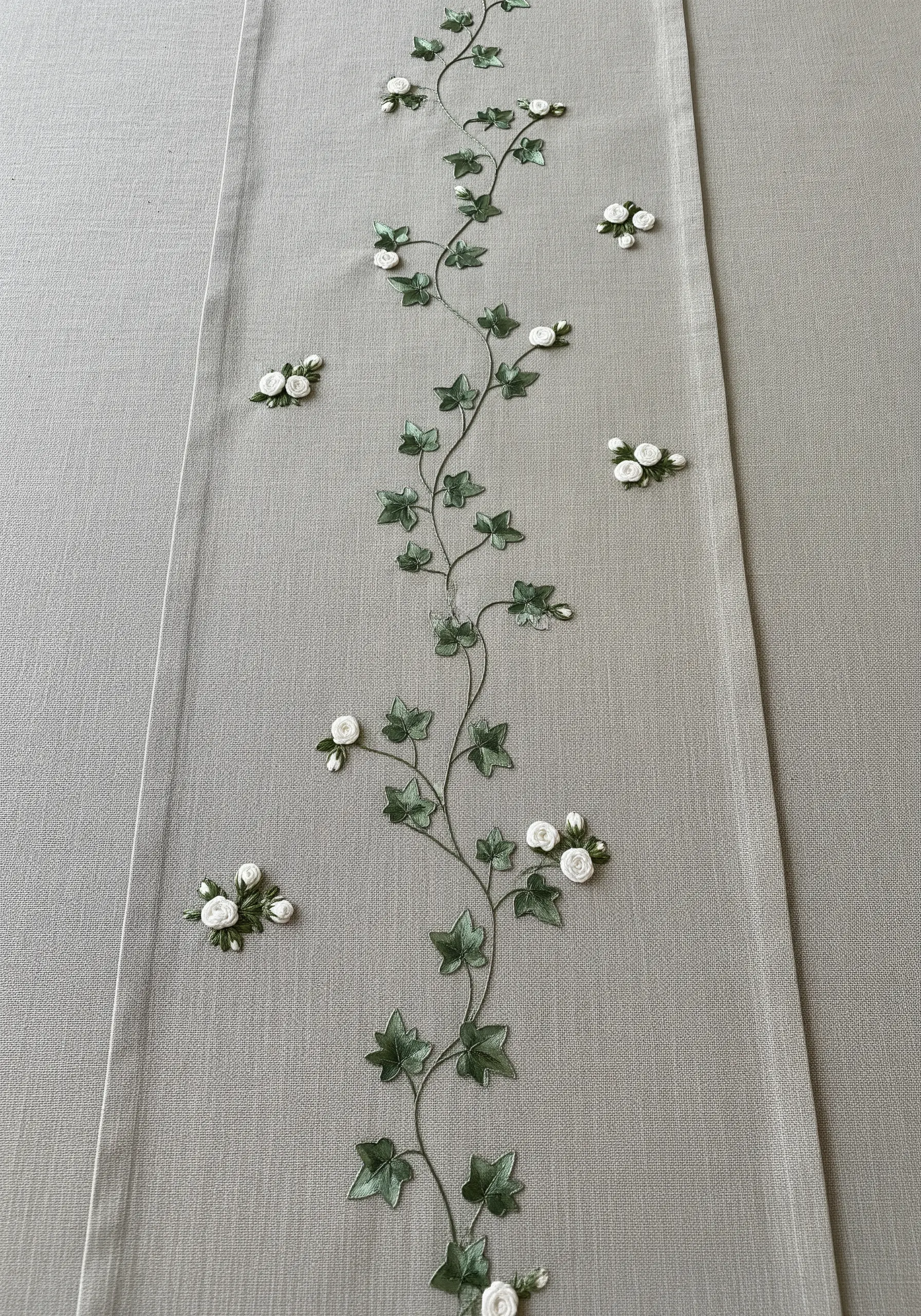 A delicate table runner embroidered with a central winding ivy vine and tiny 3D white roses.