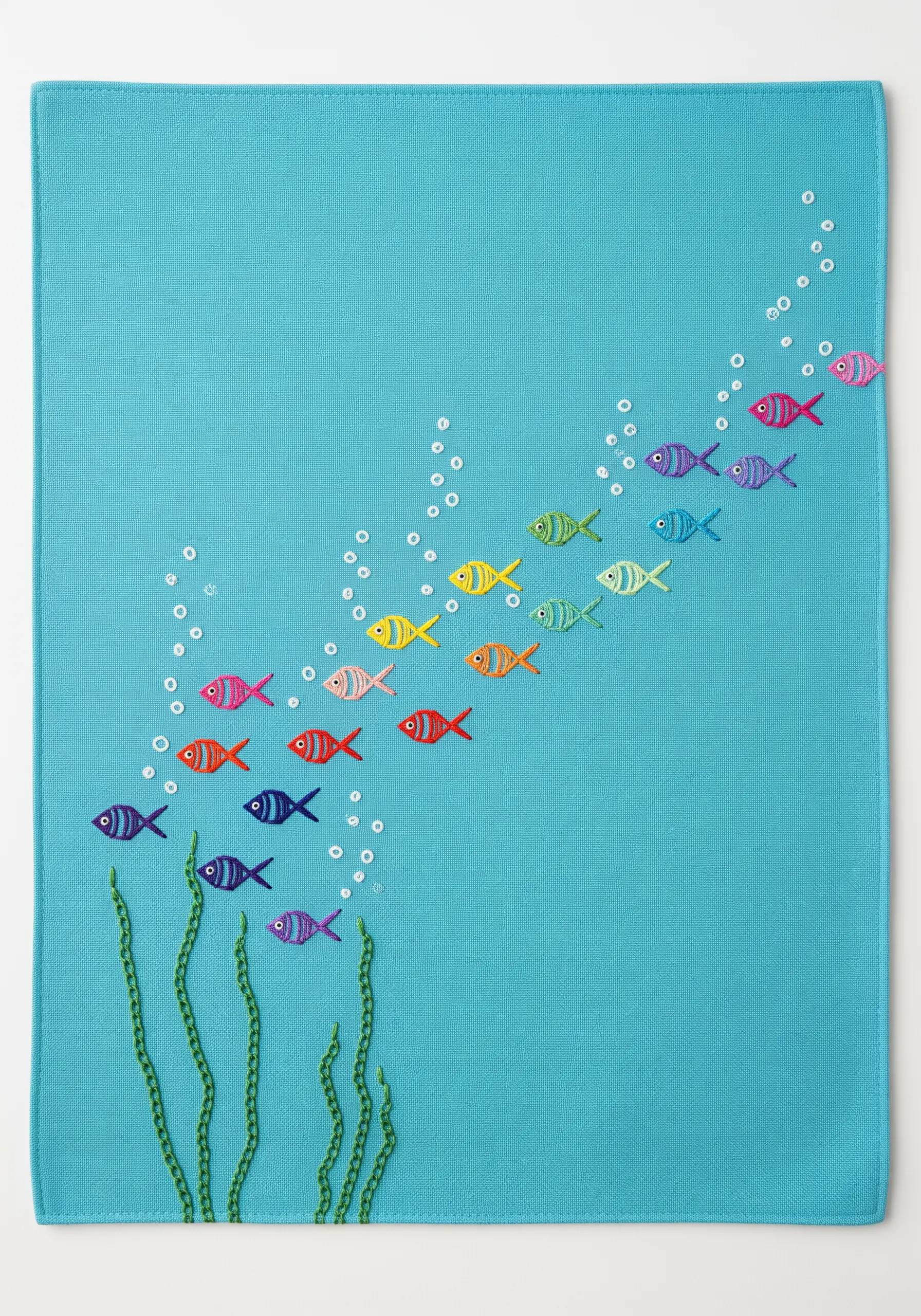 Small embroidered fish in a rainbow gradient swimming upwards on blue fabric.
