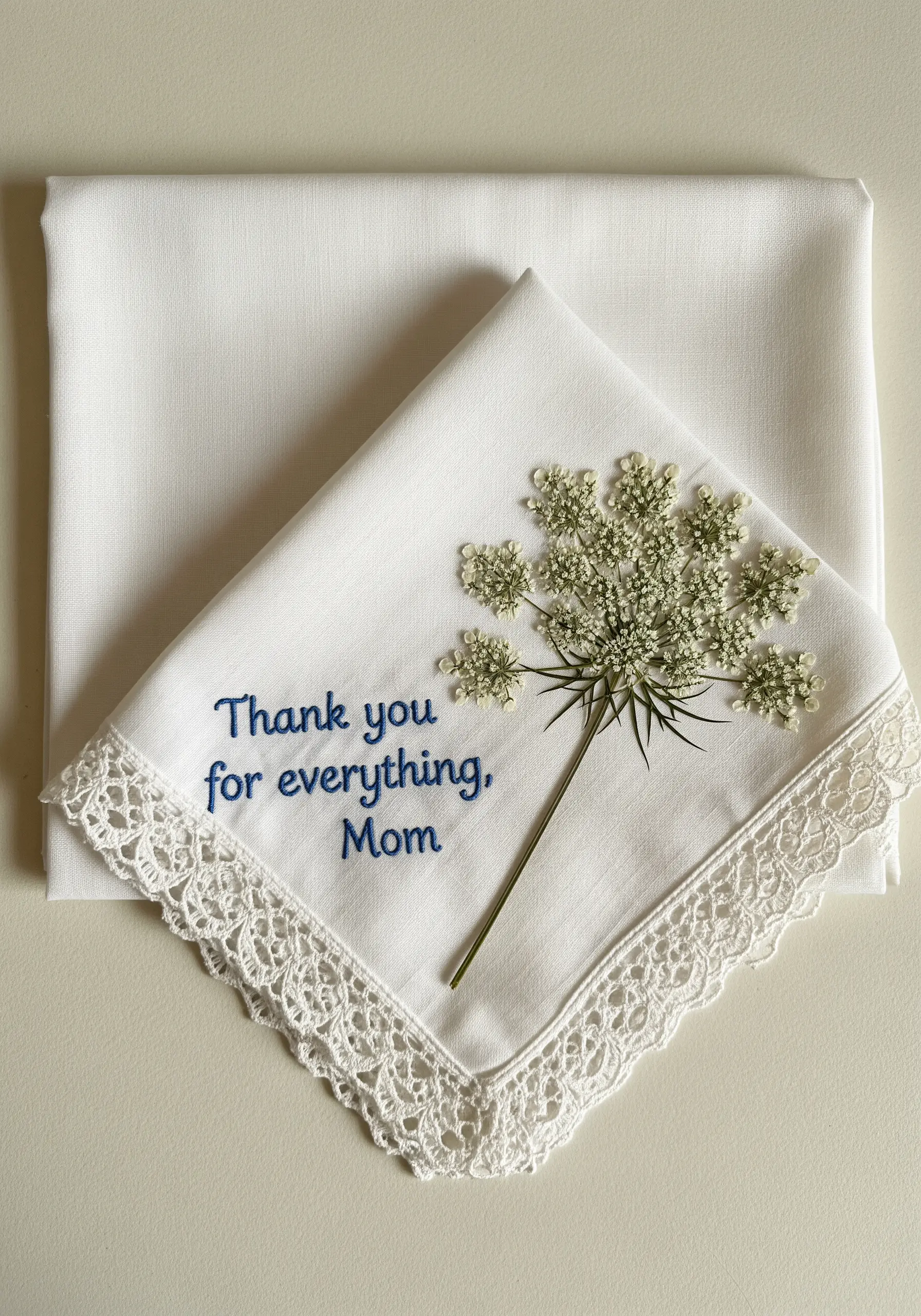 A white lace-edged handkerchief embroidered with a message and adorned with a sprig of Queen Anne's Lace.
