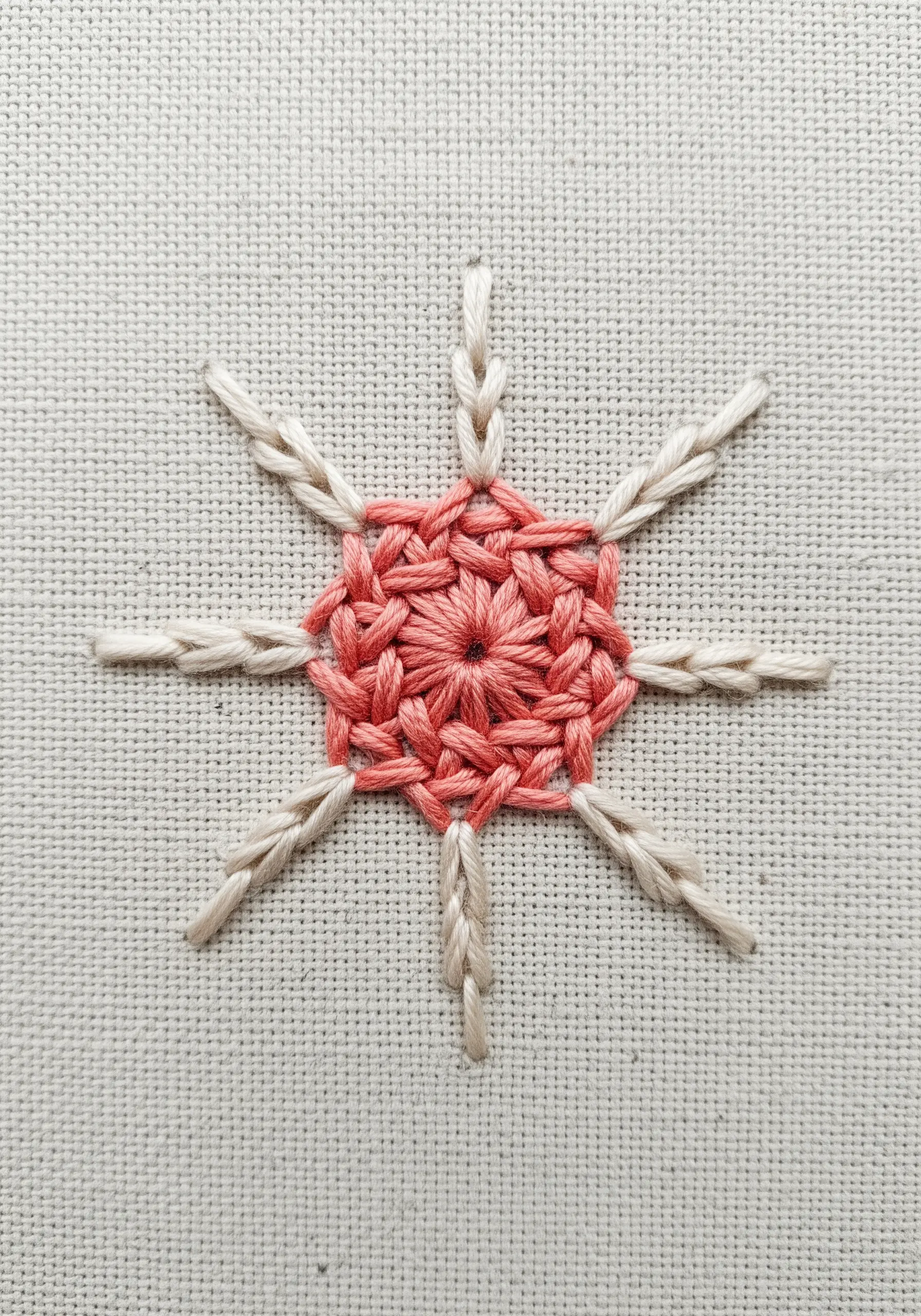 A mandala with a pink woven wheel stitch center and radiating off-white stitches.