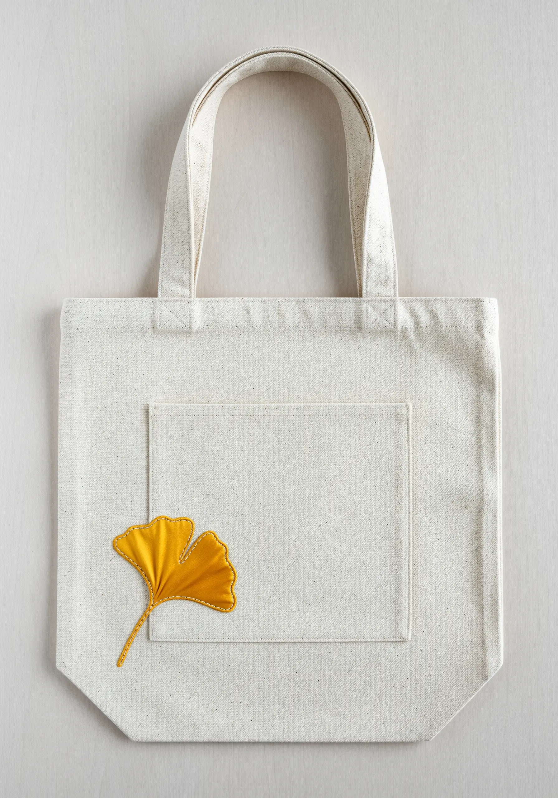 A yellow fabric ginkgo leaf appliquéd onto a canvas tote bag with a running stitch outline.