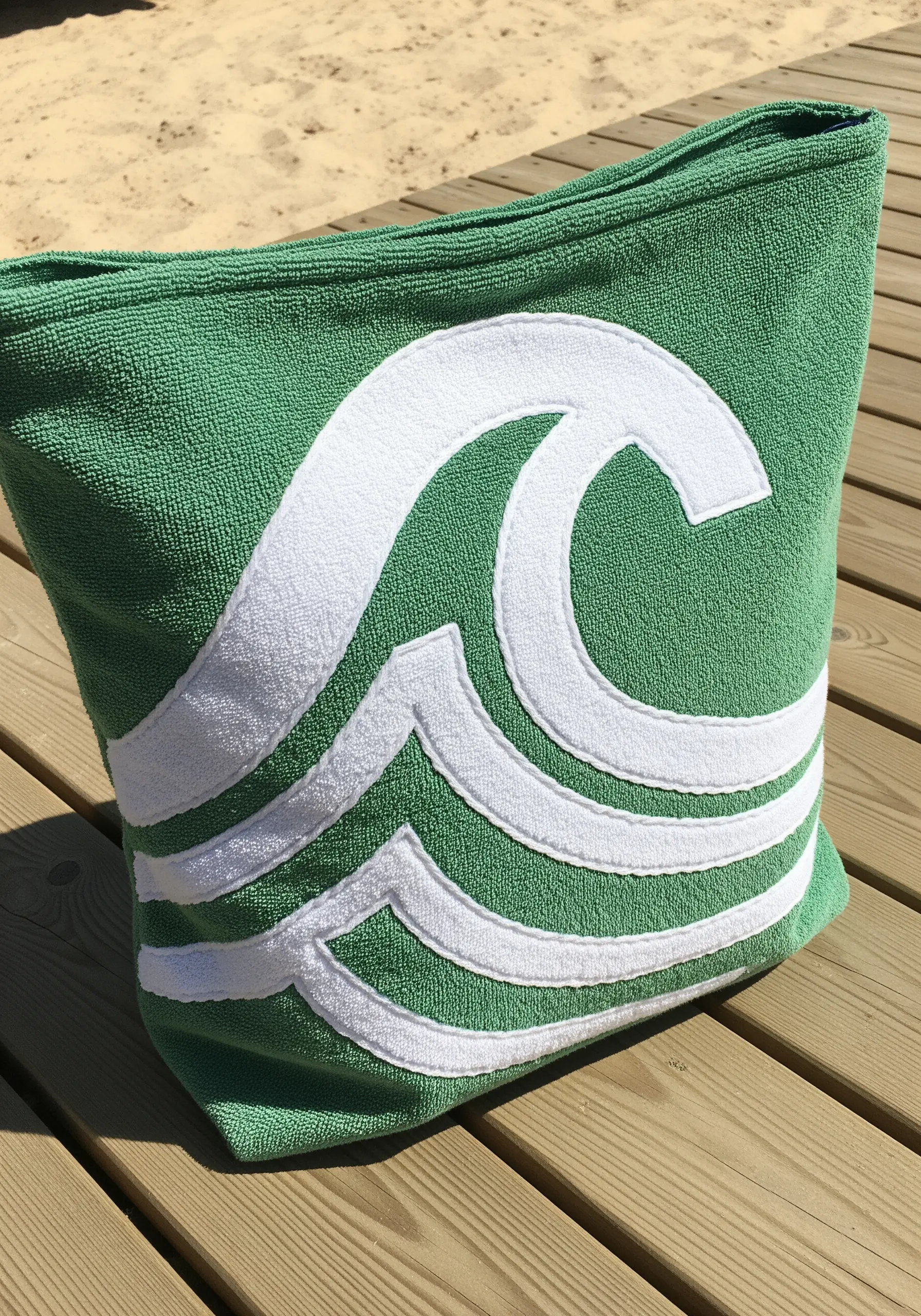 A green terrycloth tote bag with a large white wave appliqué stitched on.