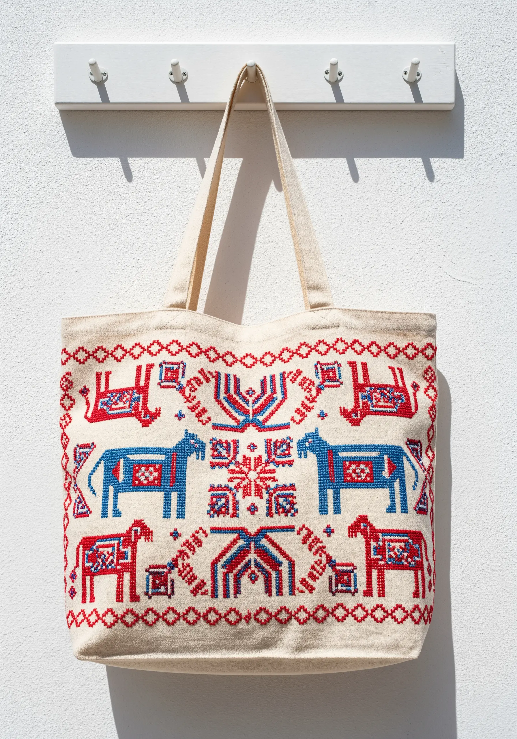 A canvas tote bag with a red and blue Scandinavian-style cross-stitch pattern of horses.