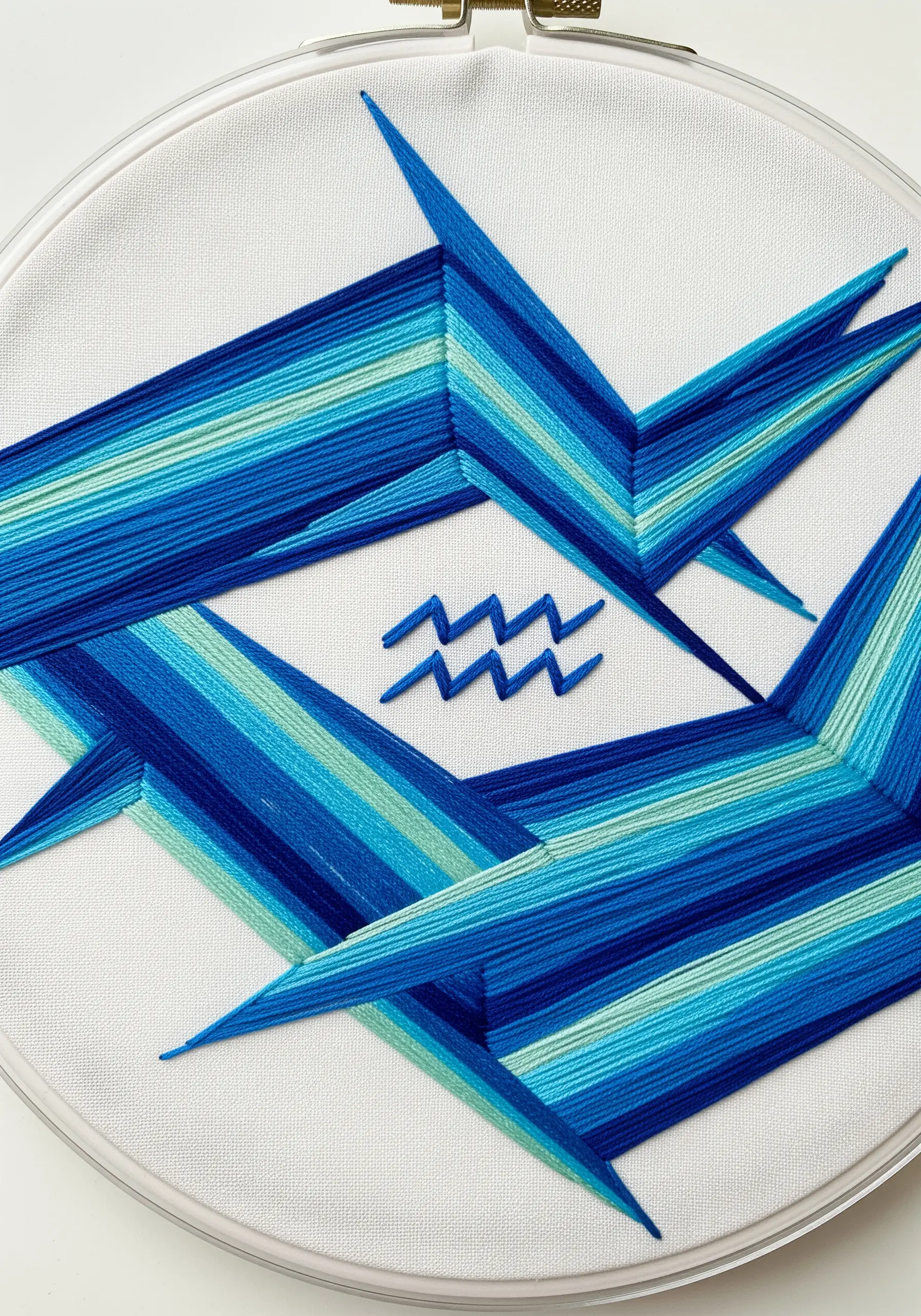 An abstract, geometric hoop art piece for Aquarius using blocks of satin stitch in shades of blue.