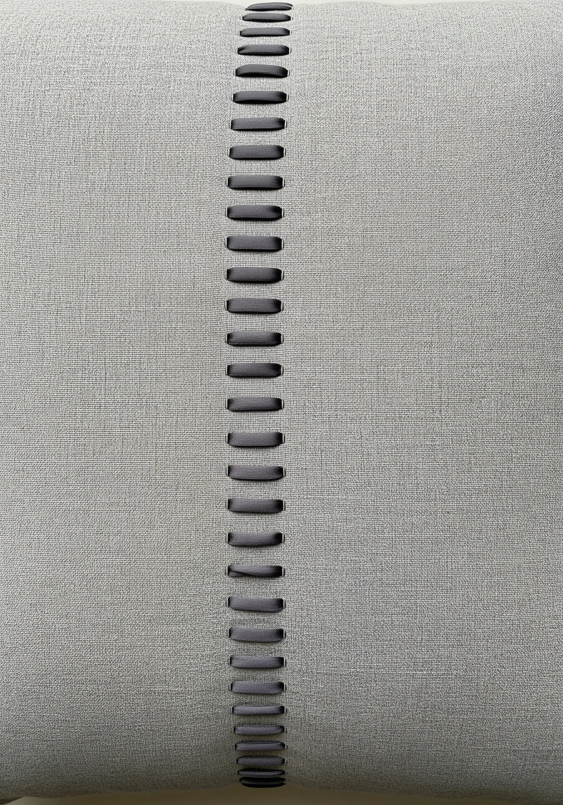 A vertical line of ladder stitch in dark grey thread on a light grey linen pillow.