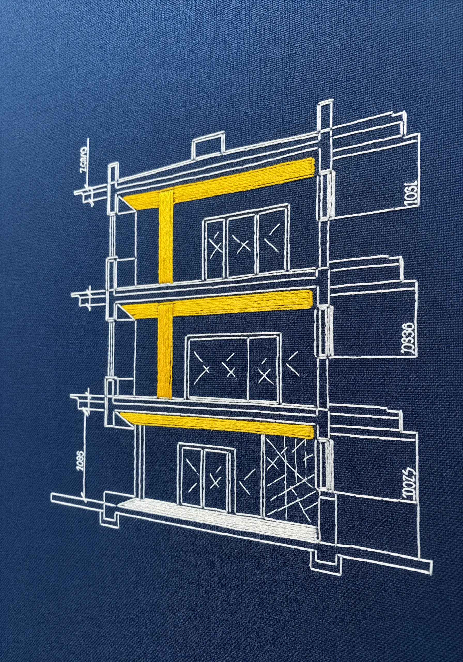 An architectural blueprint embroidered in white on navy fabric, with yellow satin stitch accents.