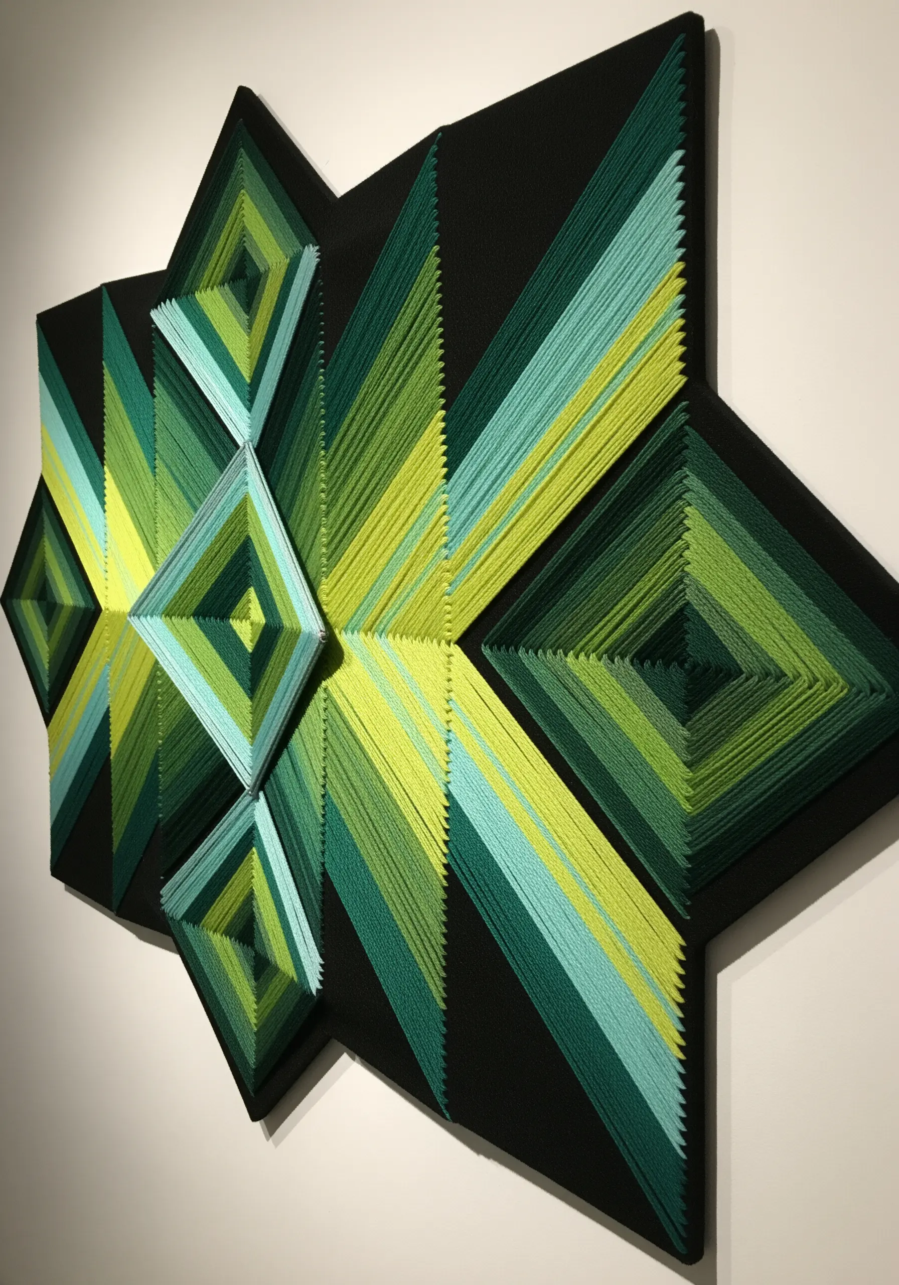 Geometric string art with green and yellow gradients on a black multi-faceted board.
