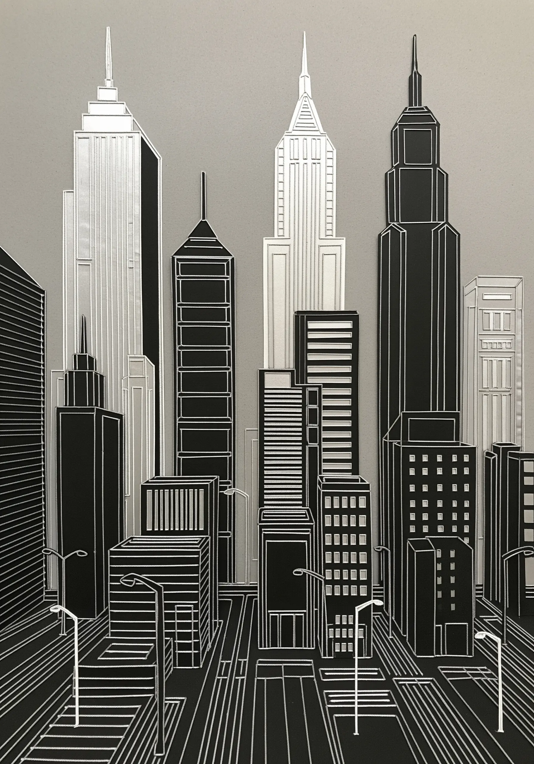 A cityscape created from precisely layered black, white, and silver paper, mimicking embroidery lines.