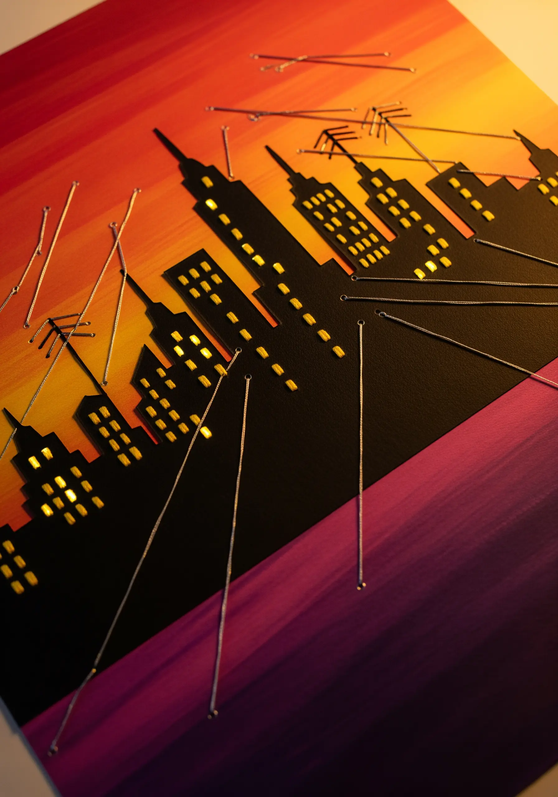 String art cityscape with a paper-cut silhouette over a sunset gradient background.