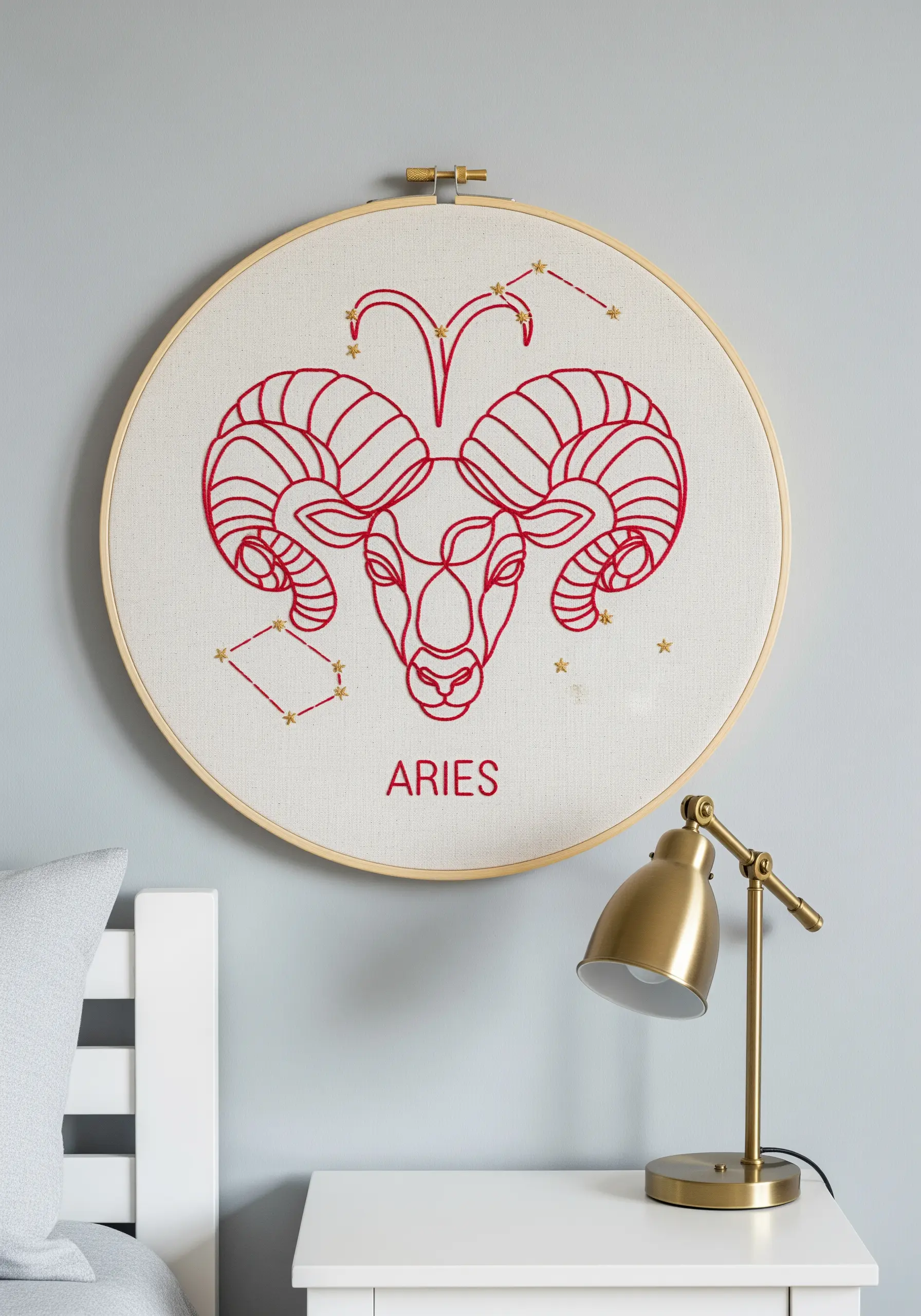 Aries zodiac sign embroidered in bold red line art on off-white fabric in a wooden hoop.
