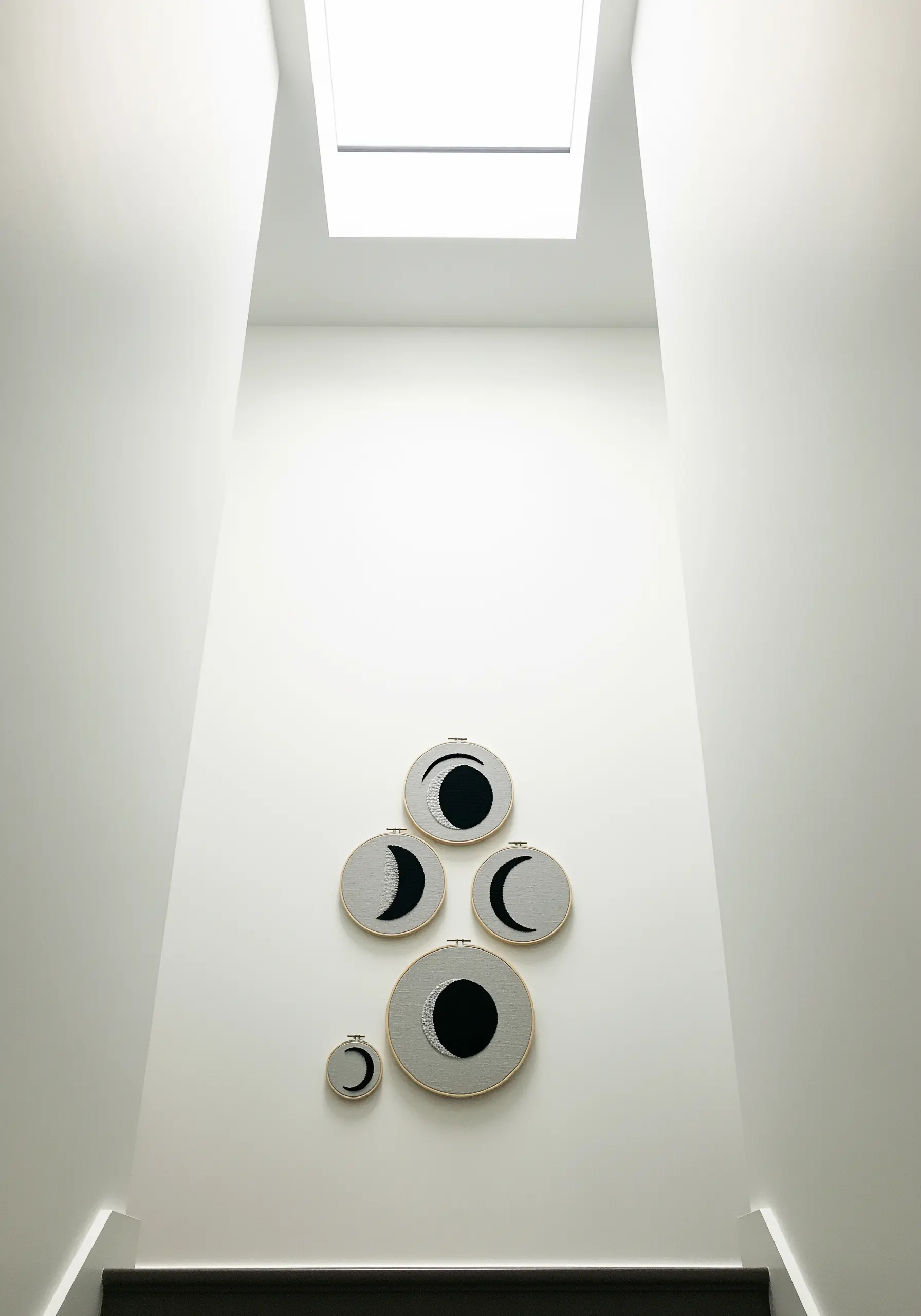 A collection of five moon phase embroidery hoops arranged on a narrow staircase wall.