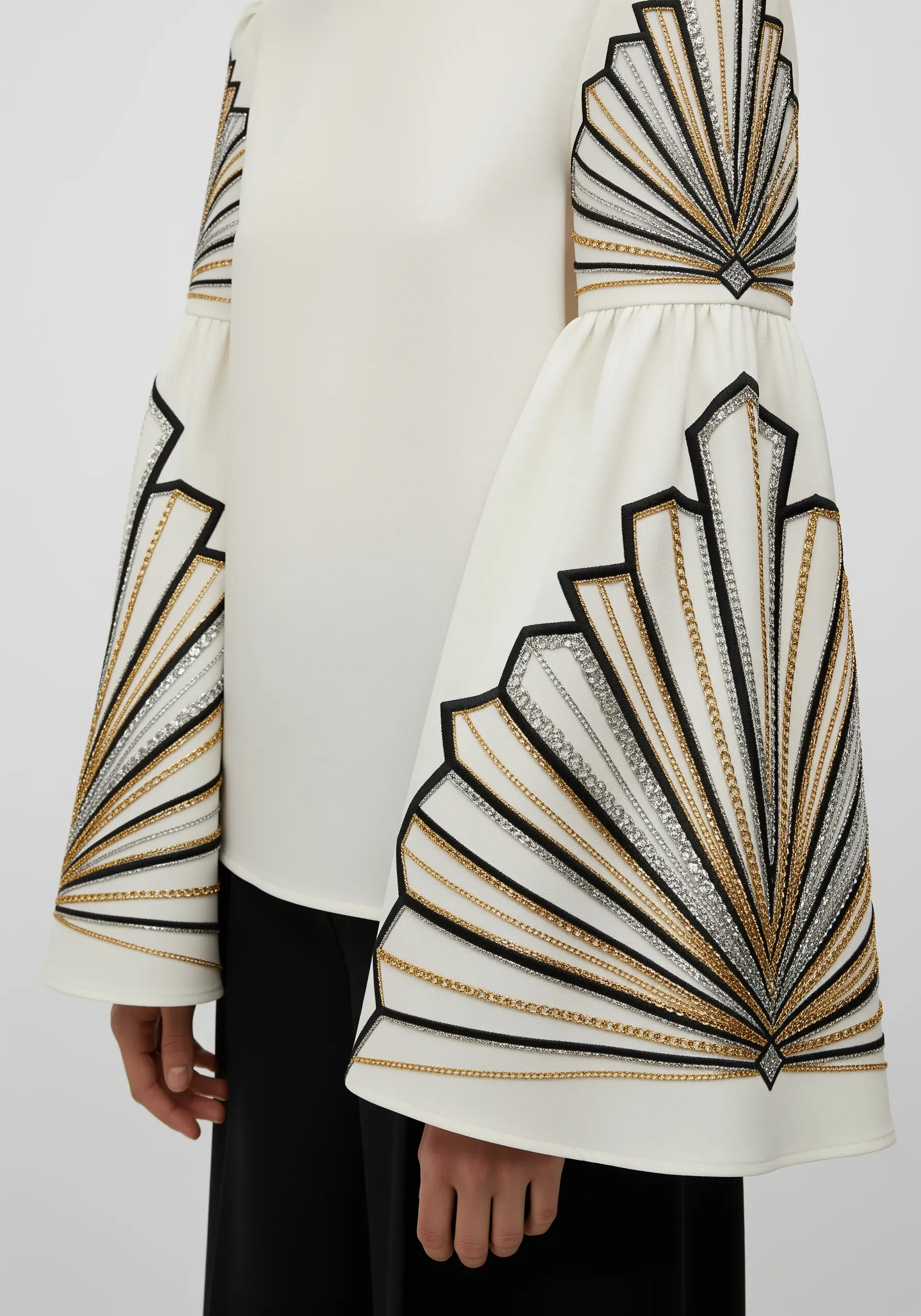 Art Deco fan design embroidered on a wide bell sleeve with black, gold, and silver threads and chains.