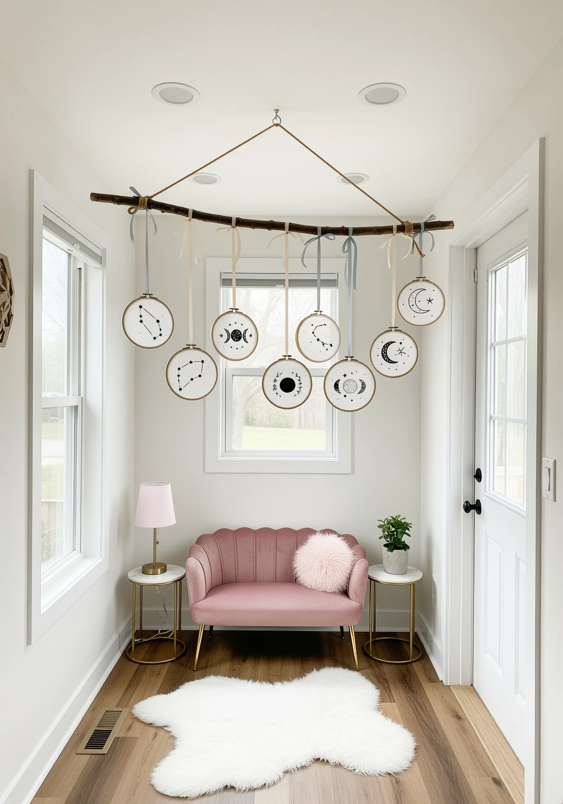 Minimalist constellation embroidery hoops hanging from a branch mobile in a white hallway.