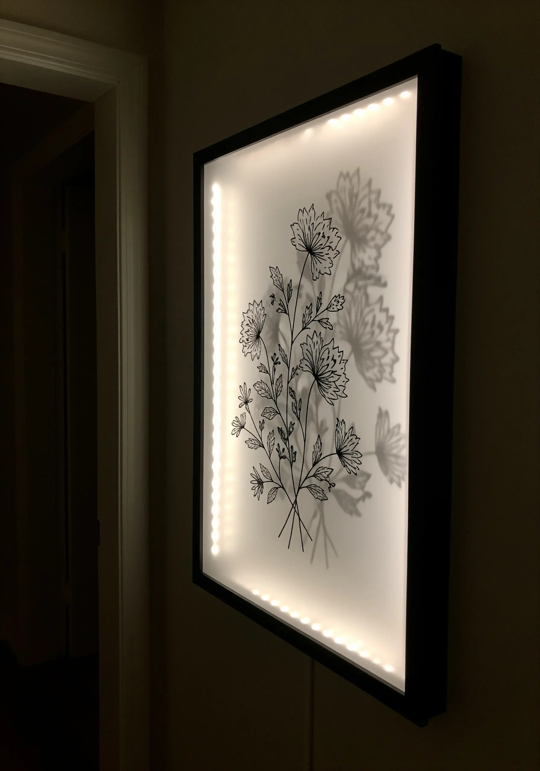 A framed piece of botanical line art embroidery, backlit with LEDs to create a shadow effect.