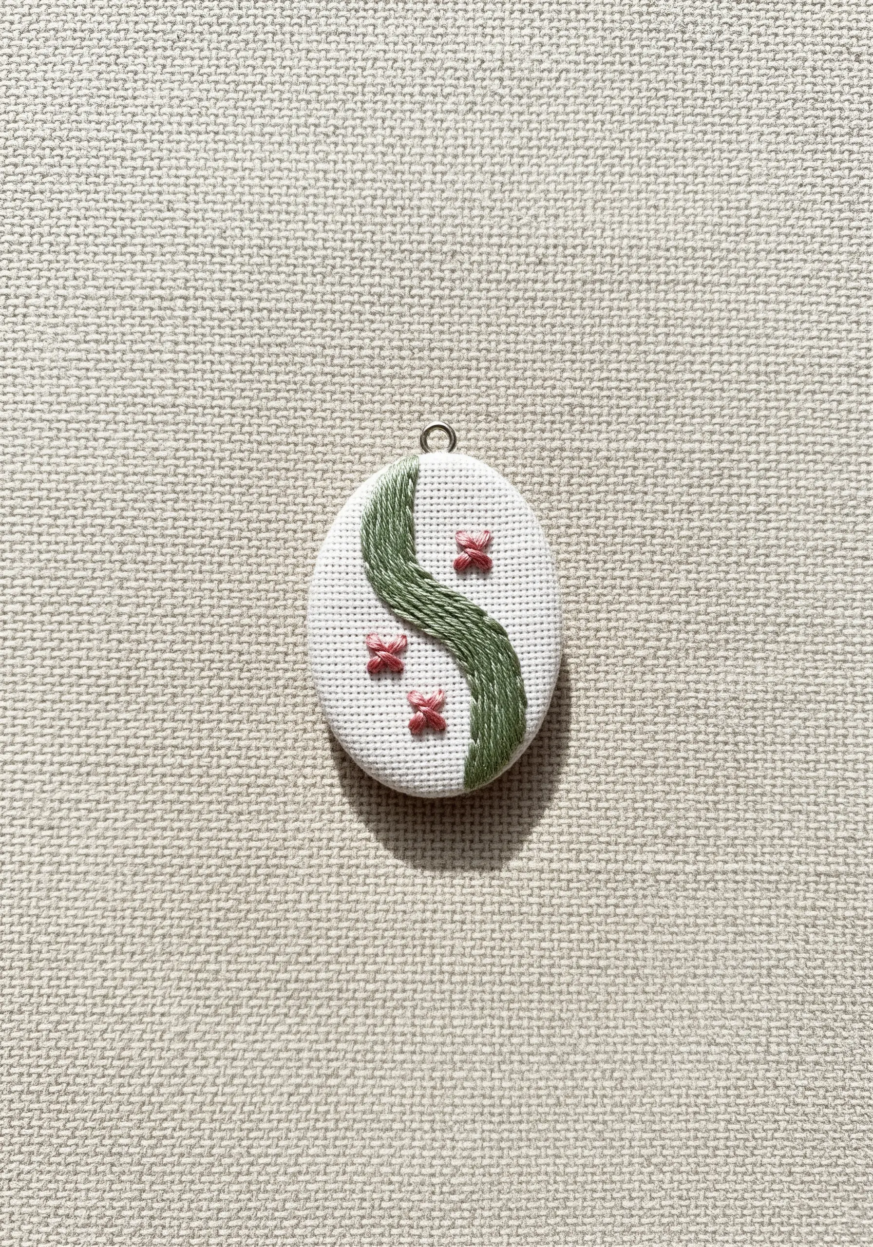 A minimalist embroidered design with a curved green stem and three pink flowers.