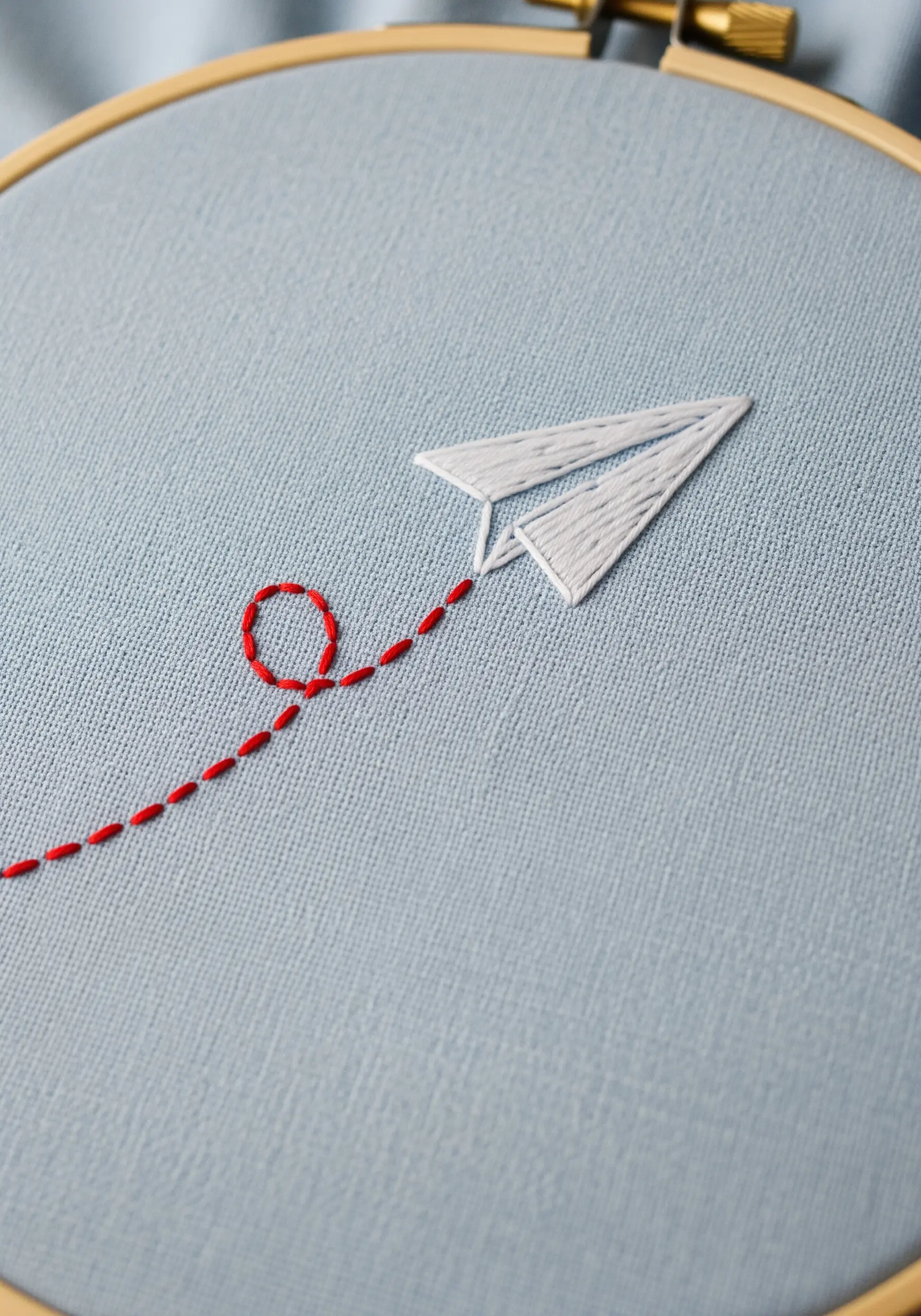 A white paper airplane with satin stitch fill and a red dashed-line flight path.