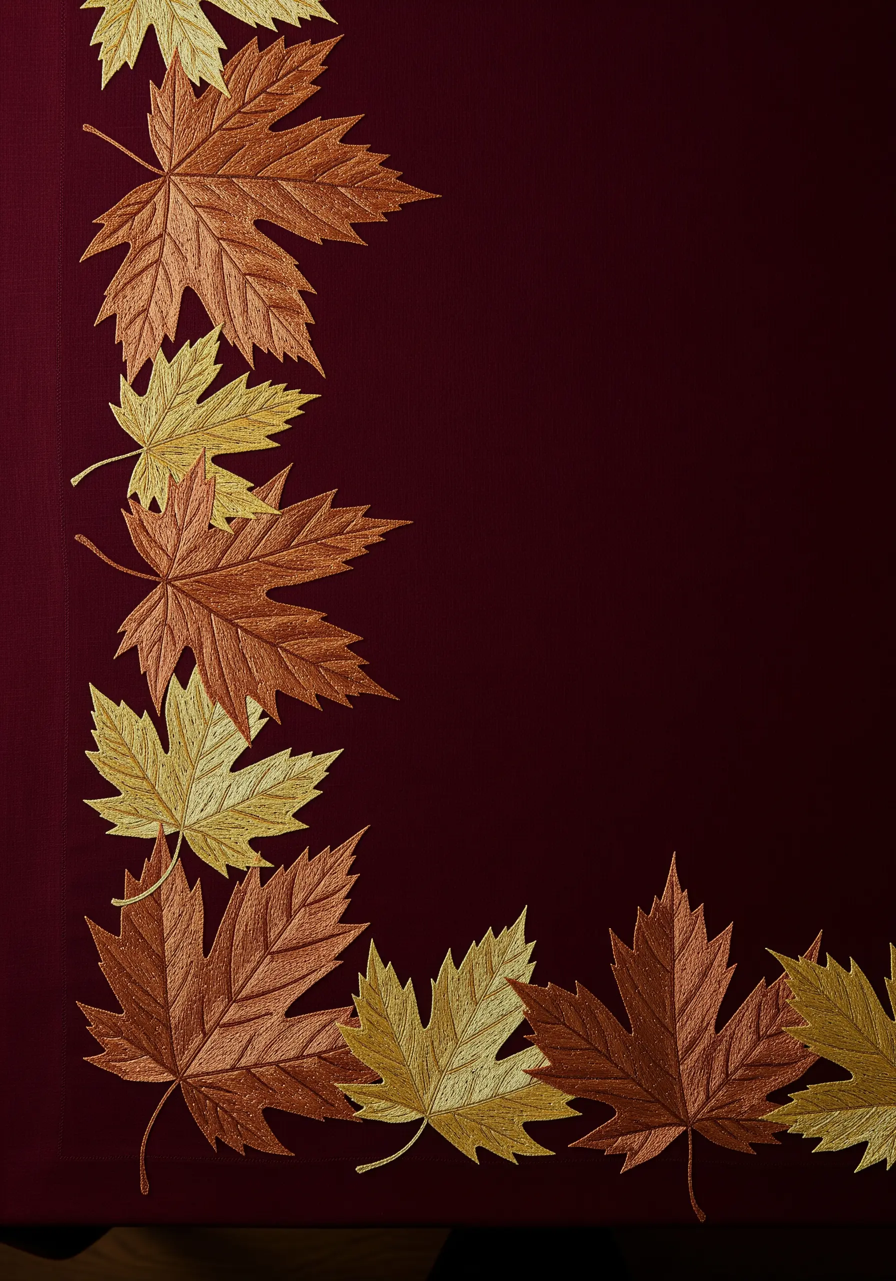 A corner design of embroidered maple leaves in metallic copper, bronze, and gold on burgundy fabric.